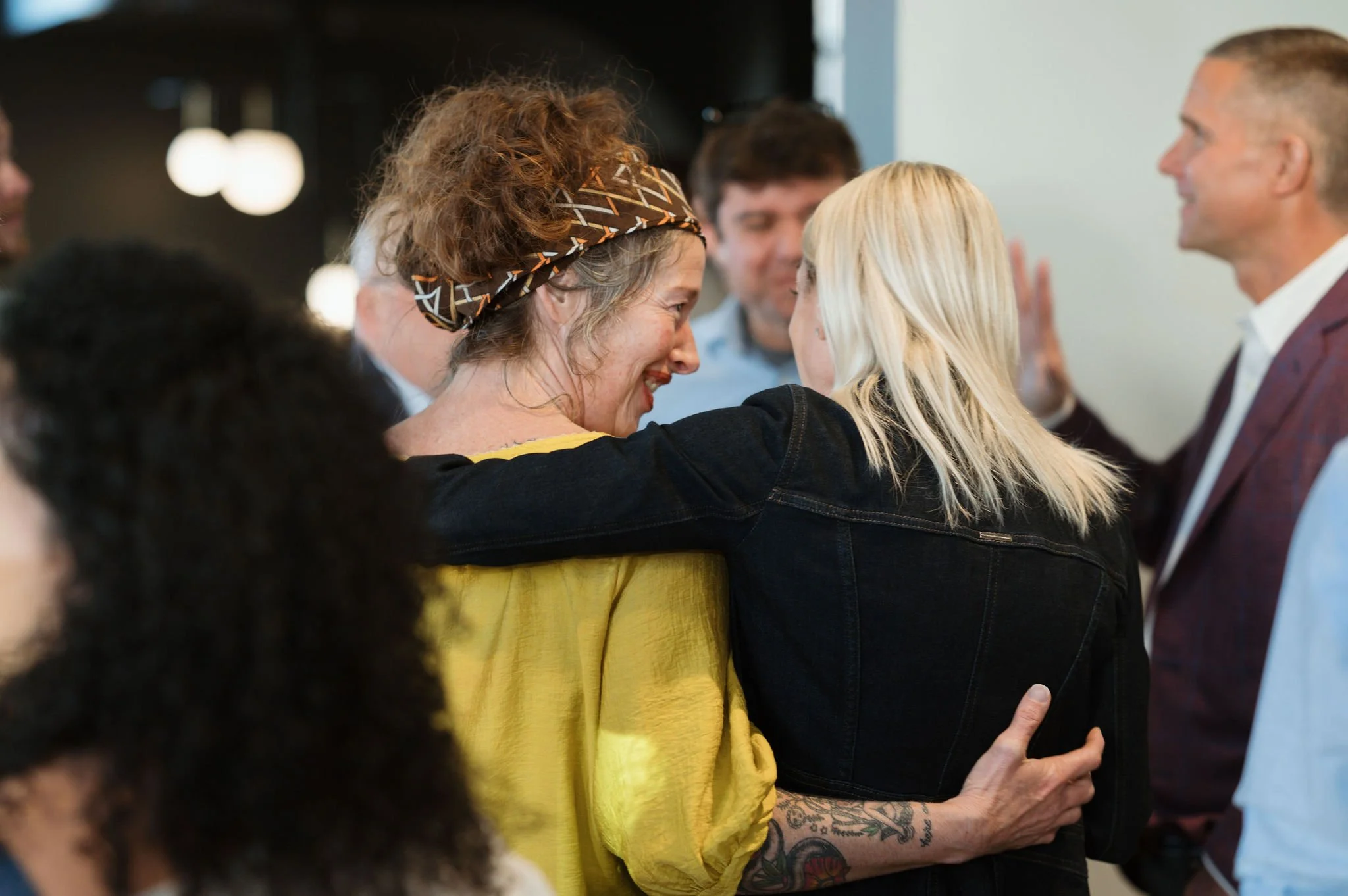 Group of people smiling and greeting each other warmly, chatting at a social gathering or event.