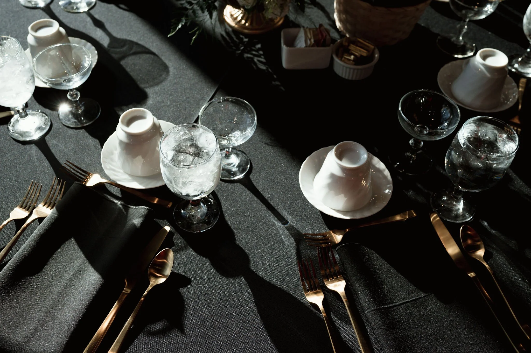 Elegant table setting with white plates, glassware, gold cutlery, and napkins, illuminated by sunlight.