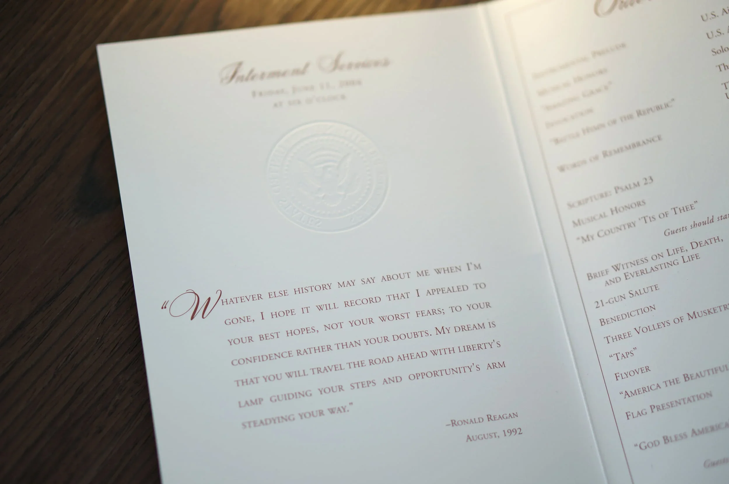 Close-up of a printed service program or flyer on a wooden surface, showing text and an embossed seal with an eagle emblem.