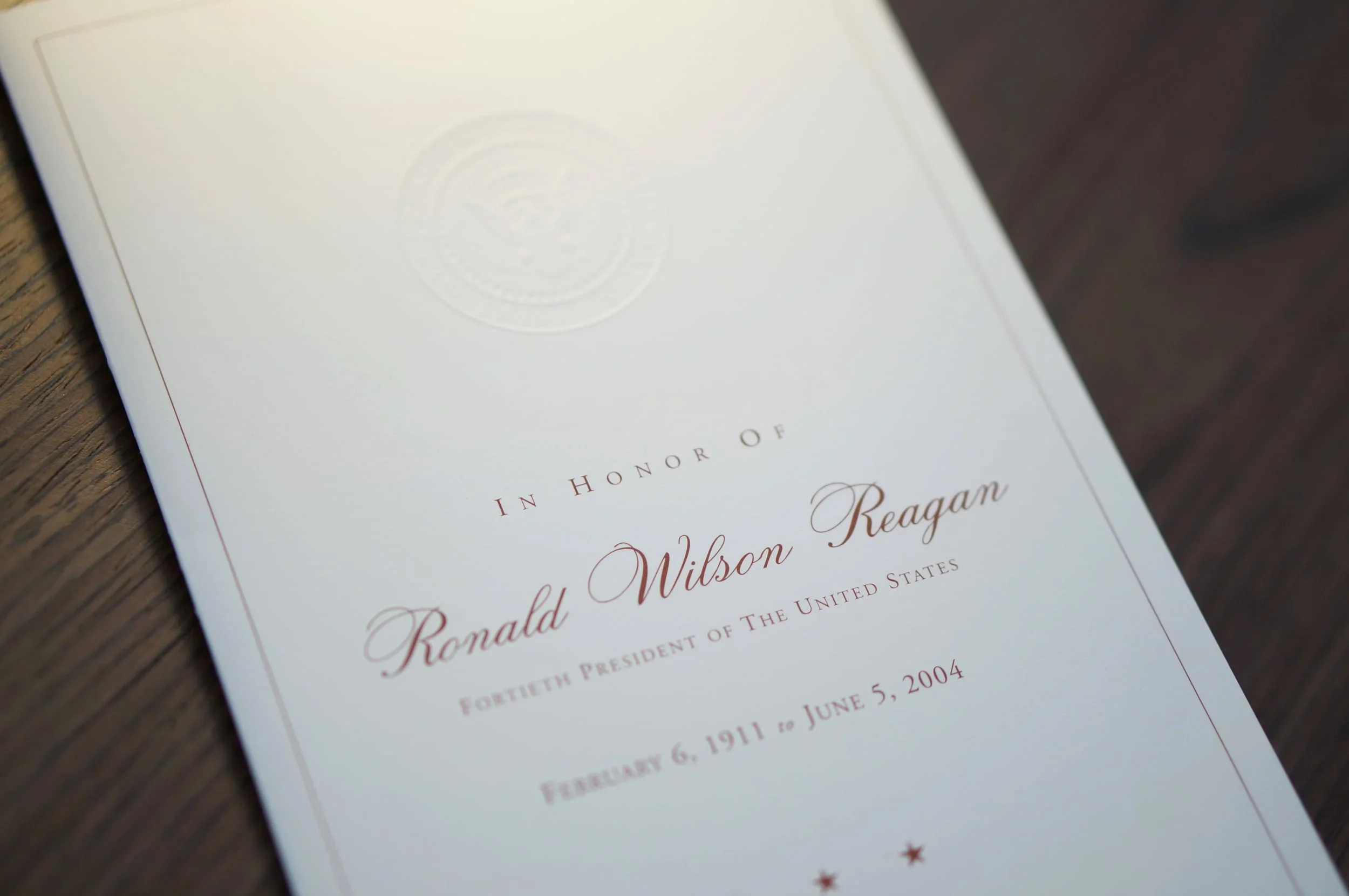 A white document with gold embossed seal and red text on a wooden surface. The document appears to be a presidential inauguration certificate for Ronald Wilson Reagan, dated June 5, 2004.