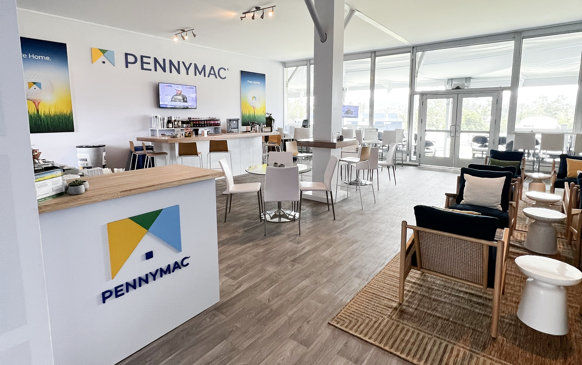 Indoor seating area at PennyMac with chairs, tables, a bar with beverages, decorative posters on the wall, and large windows letting in natural light.