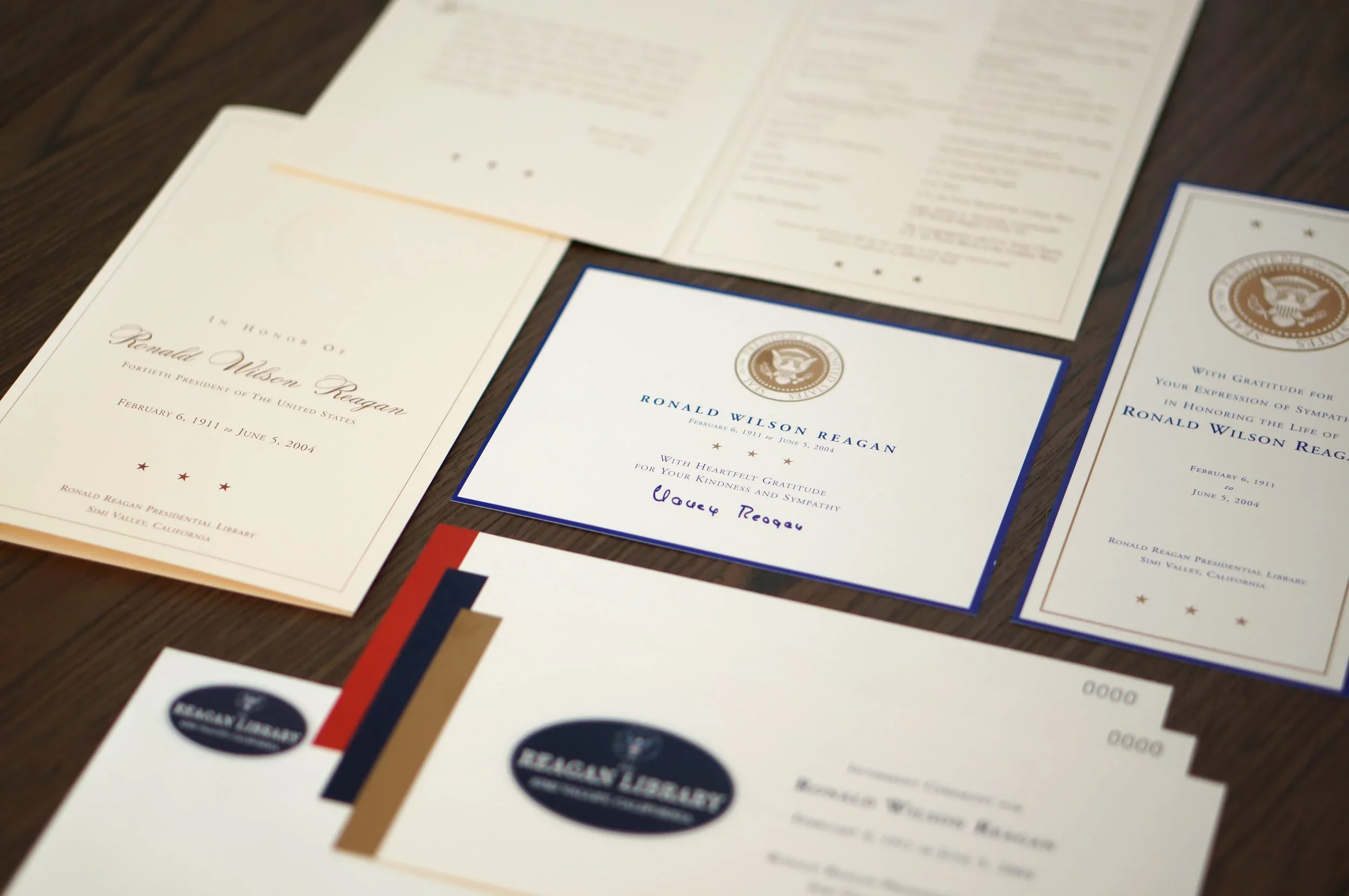 Several documents and a thank you note related to Ronald Reagan, displayed on a wooden surface, with some items overlapping, including a front cover and a letter with presidential seal.