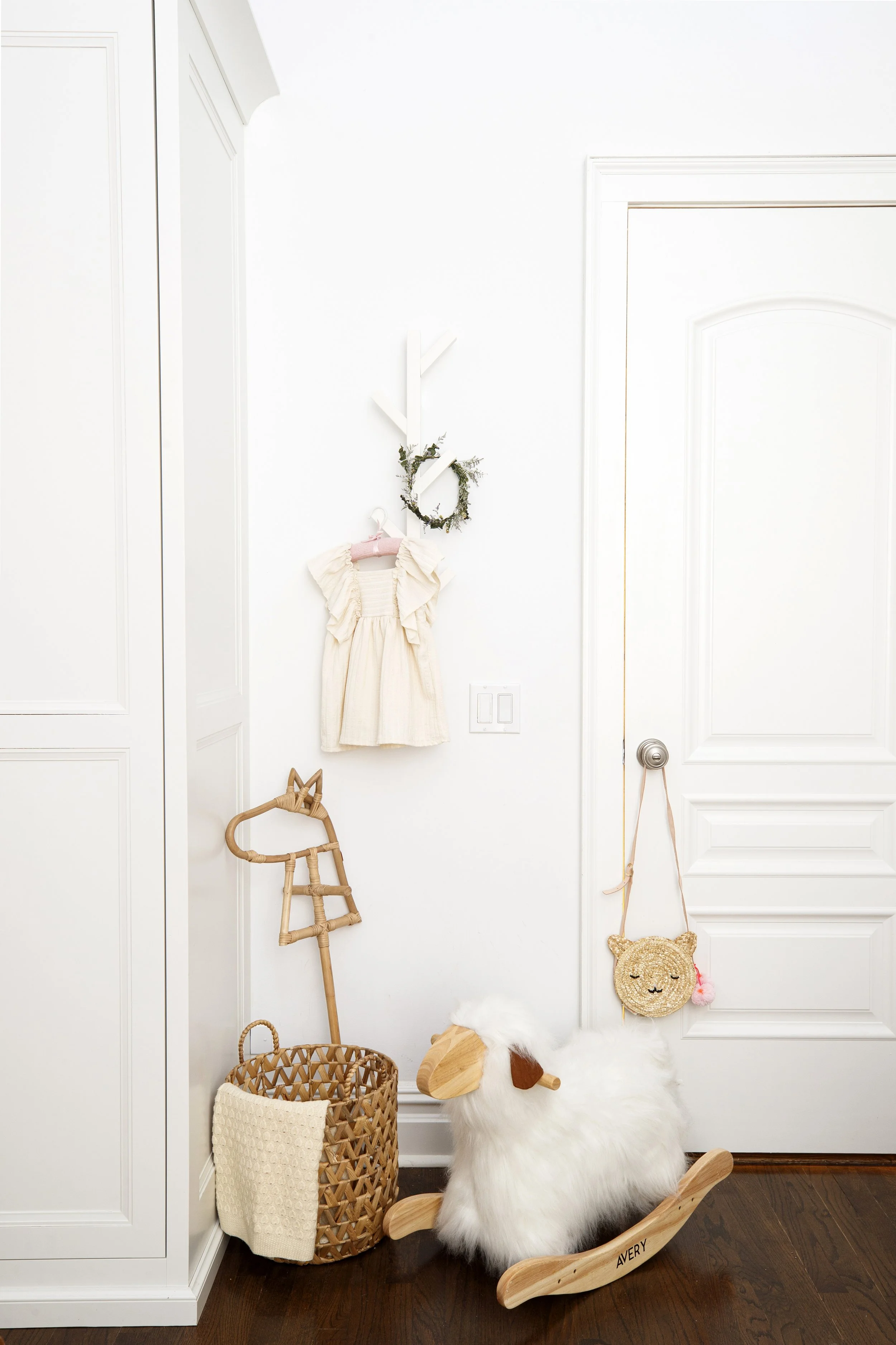 vignette featuring furry white rocking horse, cream dress and rattan basket in modern boho baby girl nursery designed by Westchester interior decorator Jordana Ross Interiors 