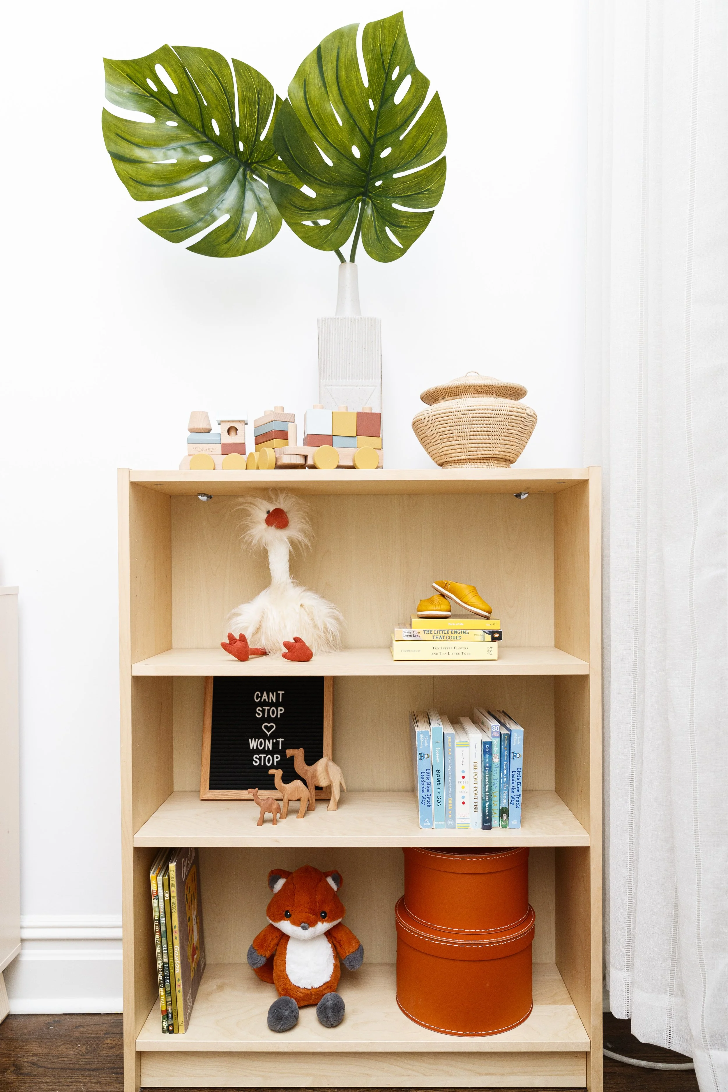wood bookshelf with colored books and toys and greenery in modern moroccan themed baby girl nursery designed by Westchester, NY interior decorator Jordana Ross Interiors 