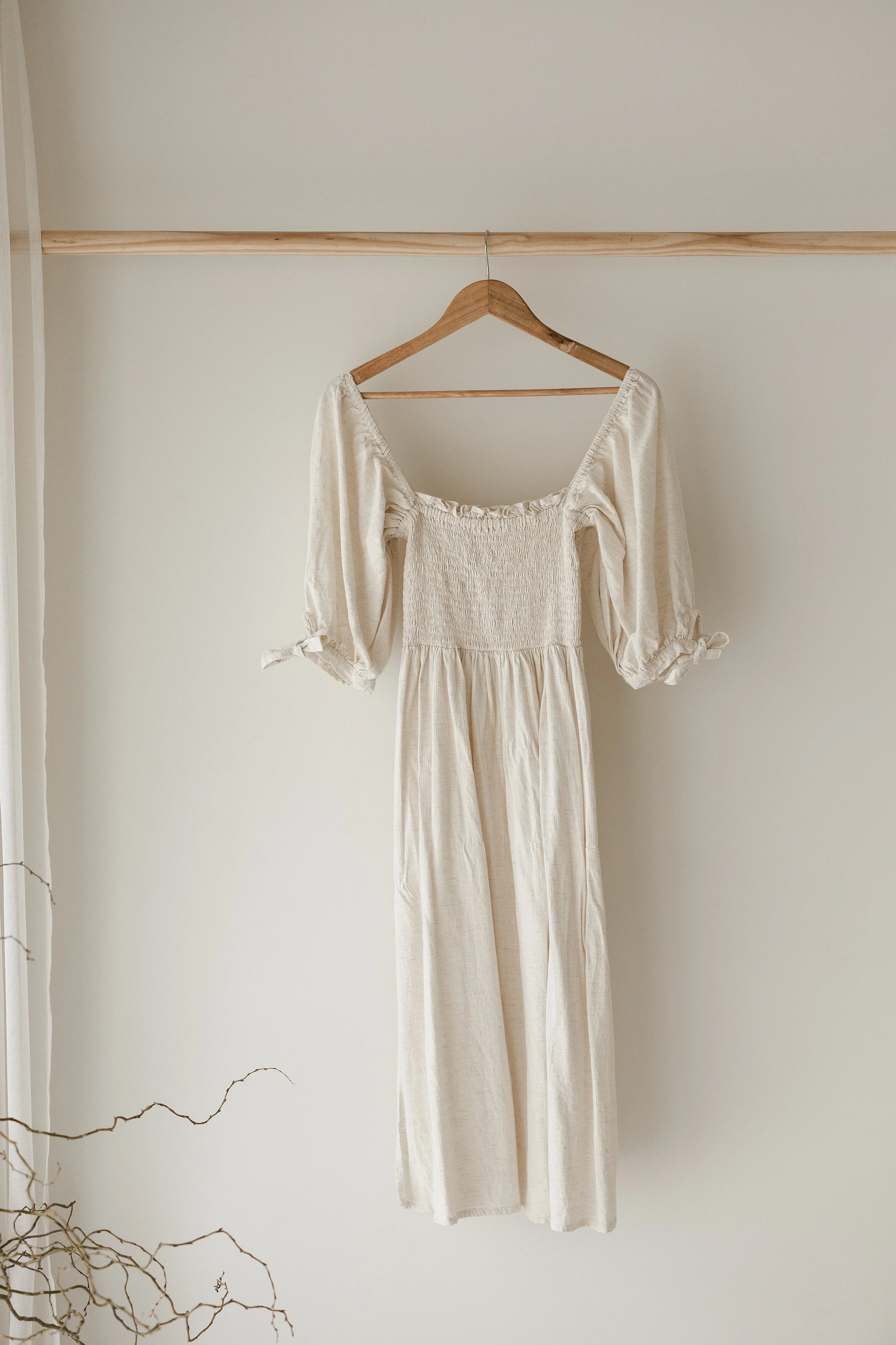 Beige long-sleeve dress hanging on a wooden hanger against a plain wall.