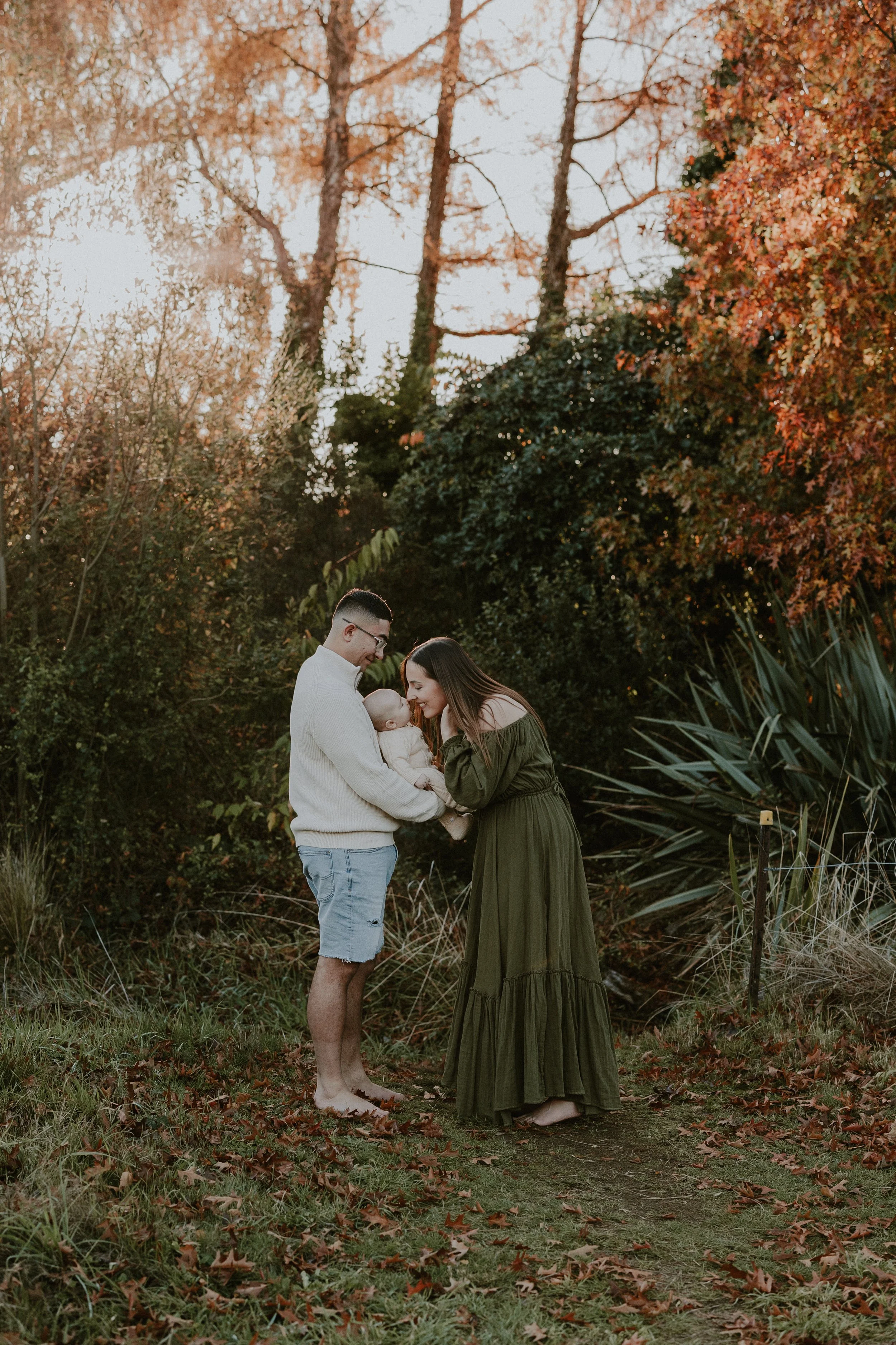 Taupo, Family Photography, Jessica Lee Photography, Waikato photographer, Mum & Dad and baby photos in a area surrounded by trees with golden light coming through, while mum is kissing baby nose