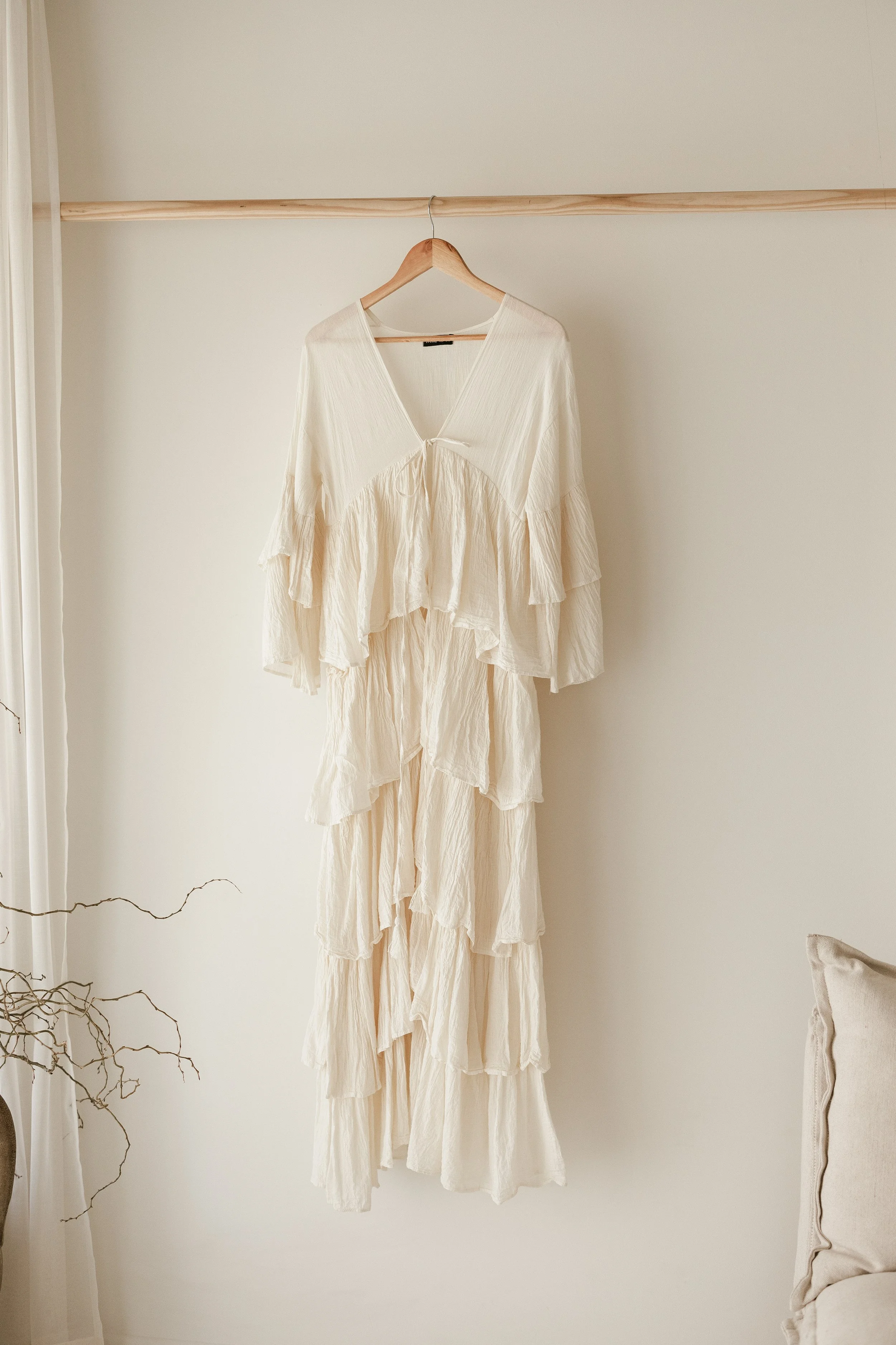 A cream-colored, layered, ruffled dress or cover-up hanging on a wooden hanger on a wall.