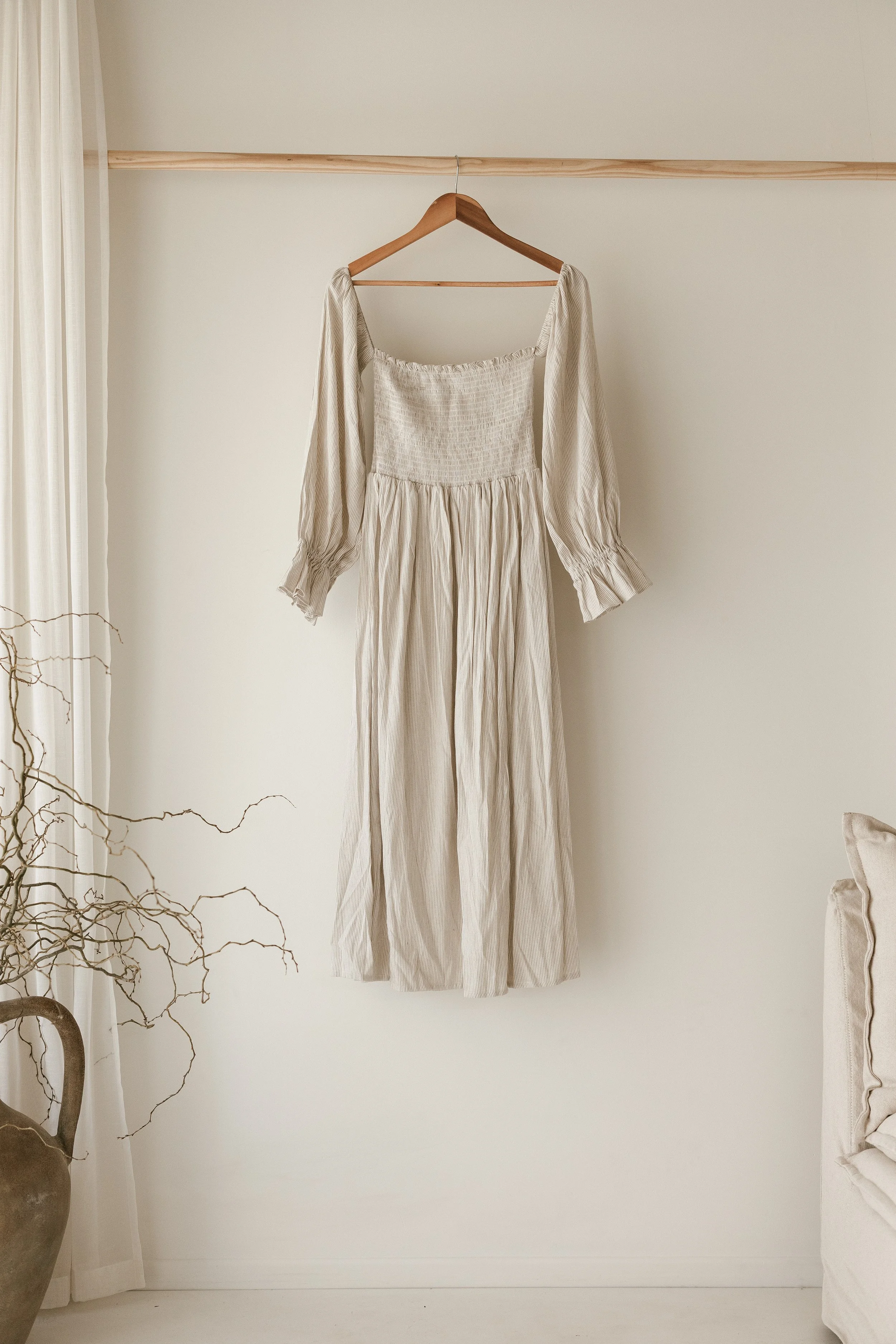Beige coloured off shoulder dress, hanging in a neutral light studio
