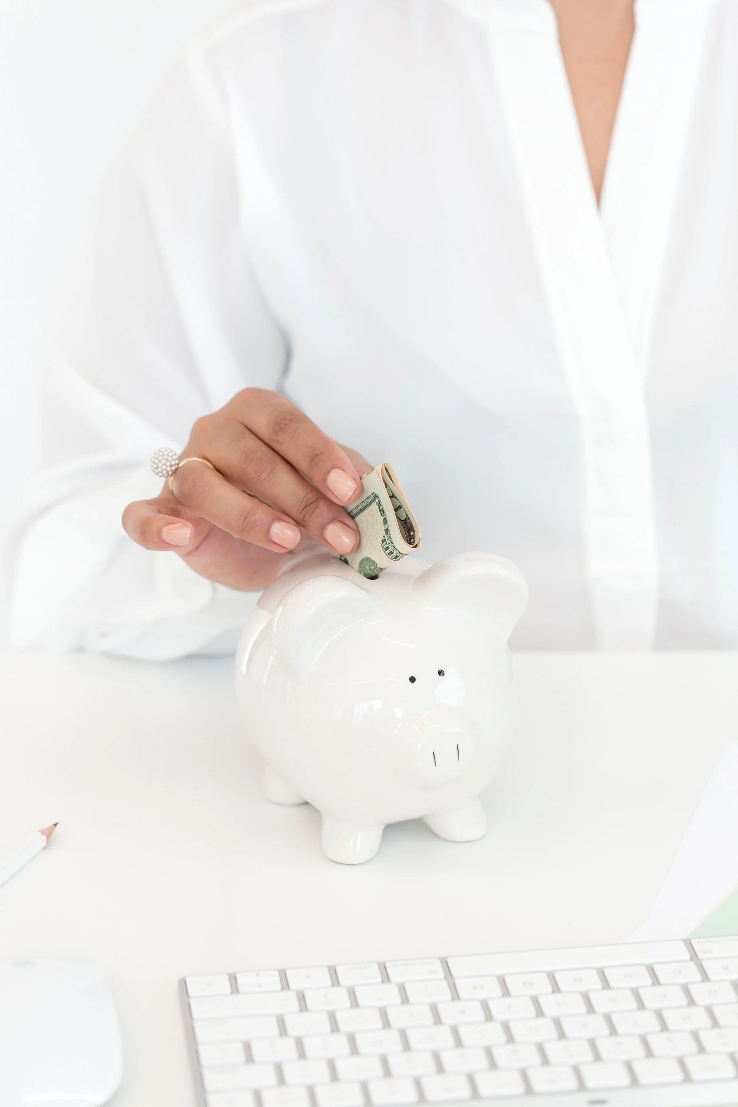 A bride-to-be placing cash into a white piggy bank, symbolizing smart wedding budgeting and financial planning.