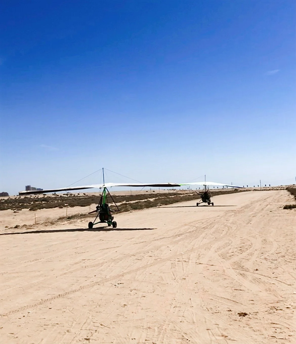 Two ultralight aircraft on a sandy dirt runway under a clear blue sky.