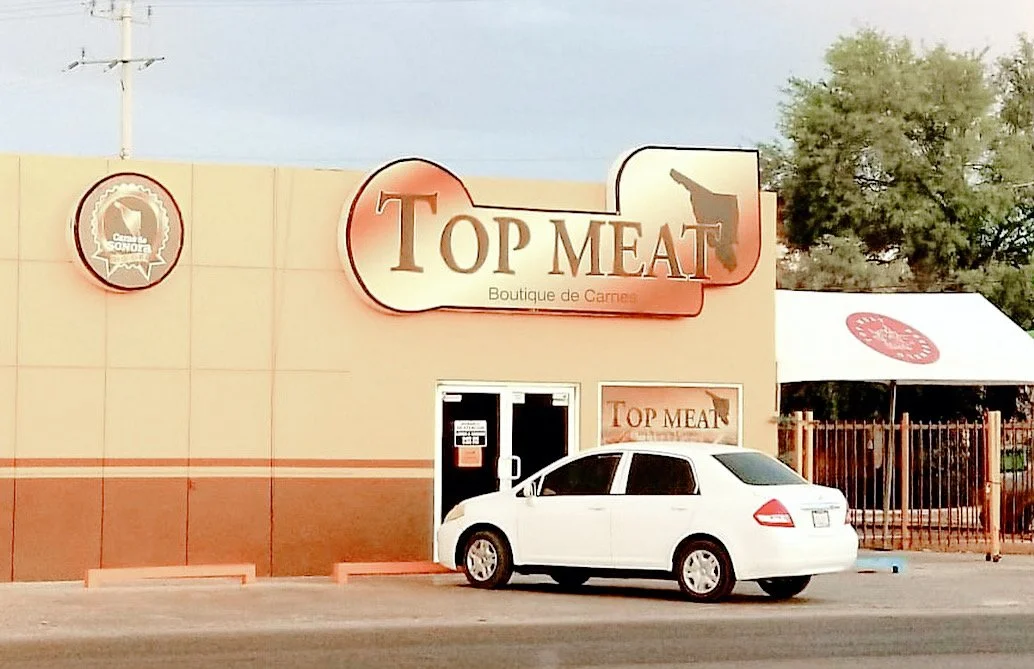 Exterior of Top Meat boutique with a sign and parked white car in front.