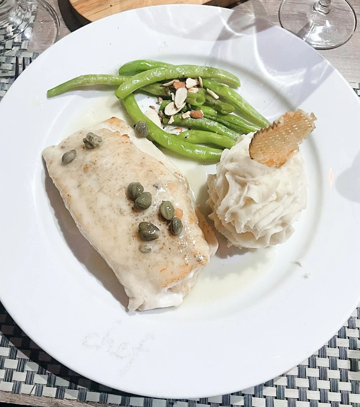 Plate with fish fillet topped with capers, mashed potatoes, and green beans with almonds.
