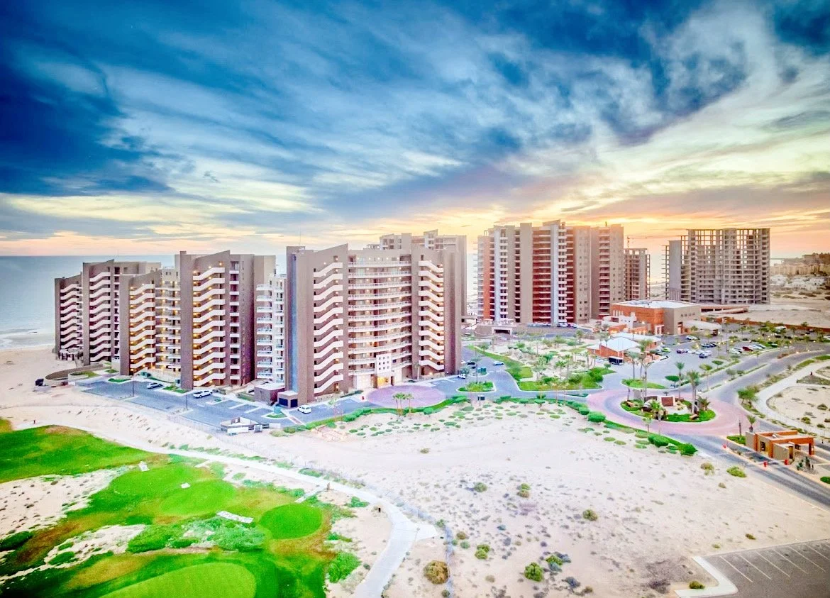 Beachfront resort complex with multiple high-rise buildings and surrounding landscaped areas during a sunset.