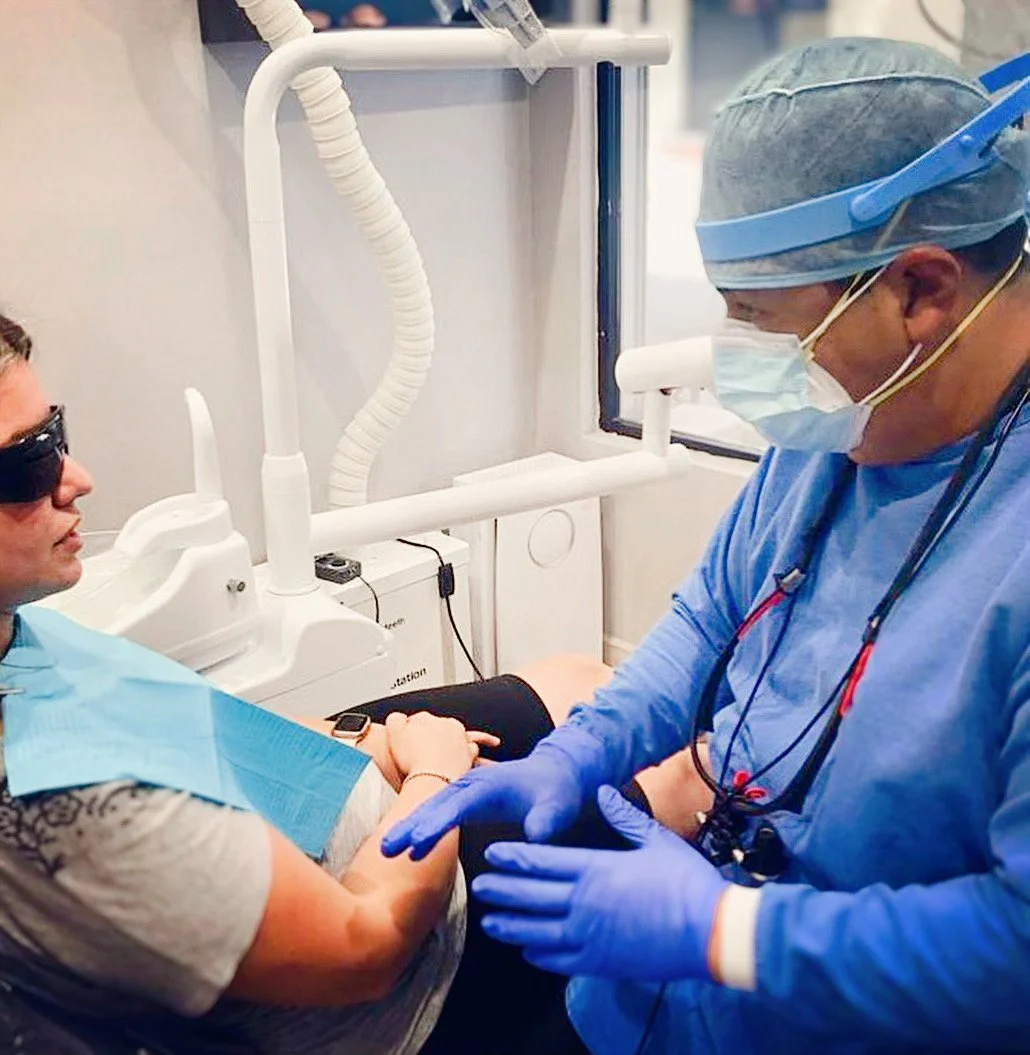 Dentist wearing gloves and mask talking to a patient in a dental chair.