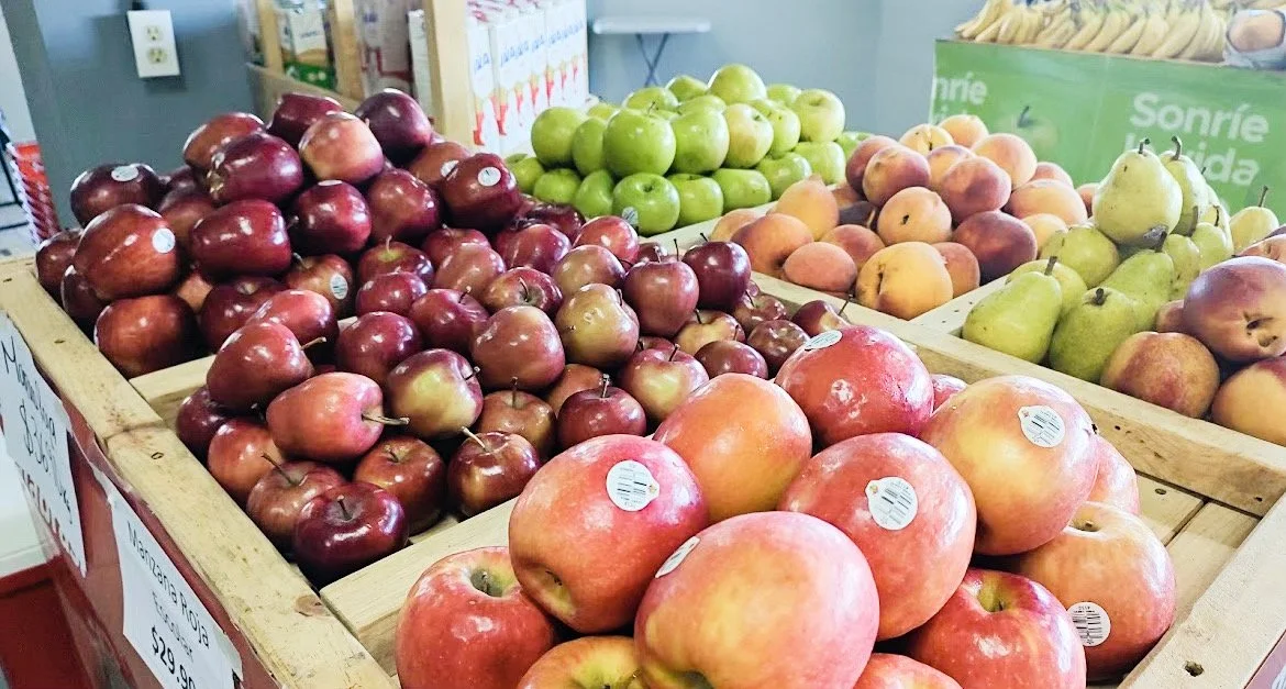 Assorted fruits on display in a grocery store, including red apples, green apples, pears, peaches, and bananas.