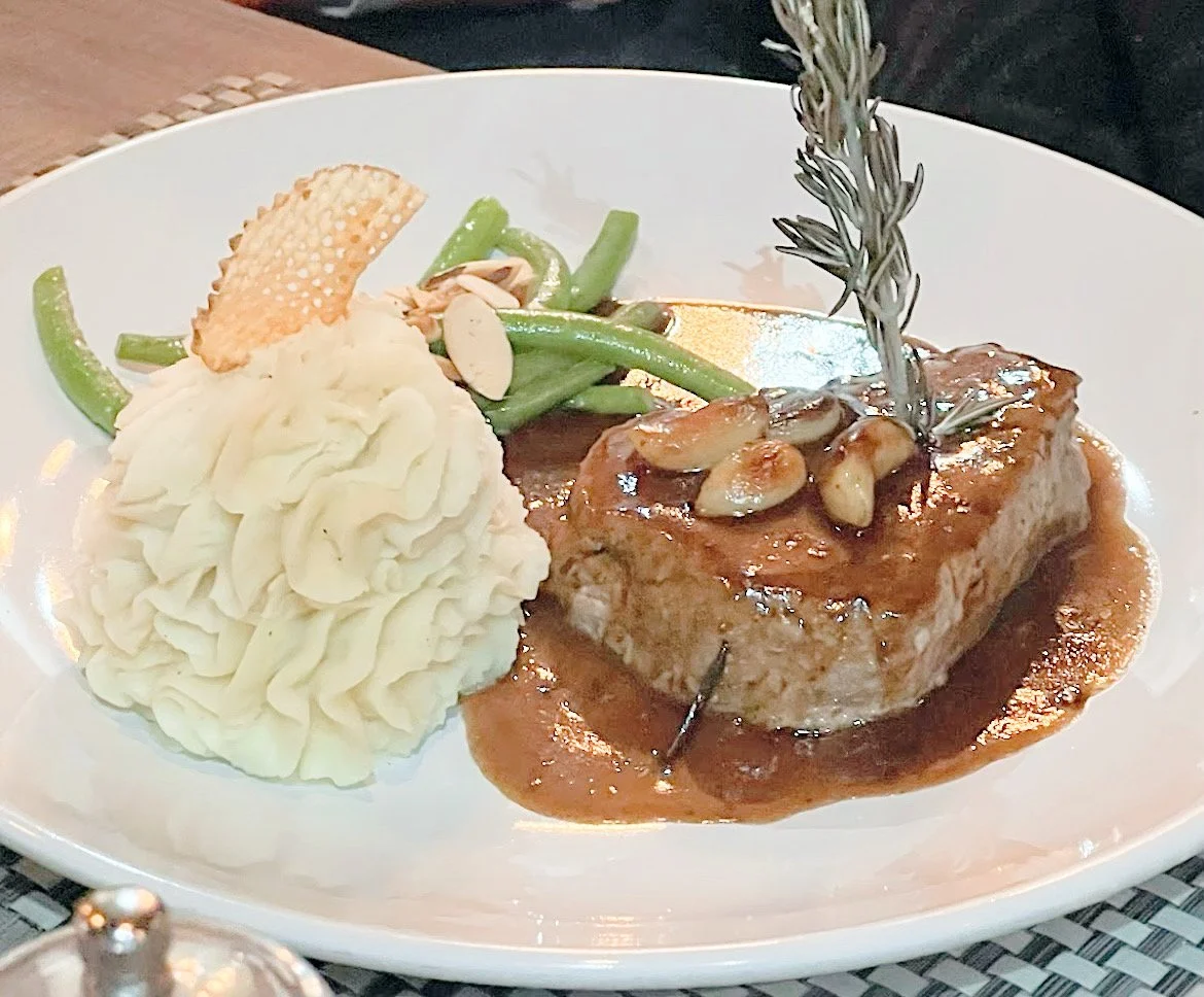 Gourmet dish with mashed potatoes, green beans, and roasted meat with sauce and rosemary.