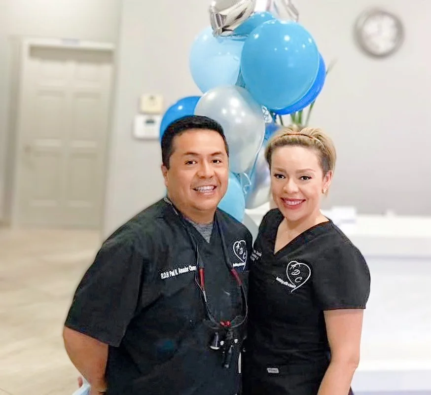 Two people in dark scrubs smiling in an office setting with balloons in the background.