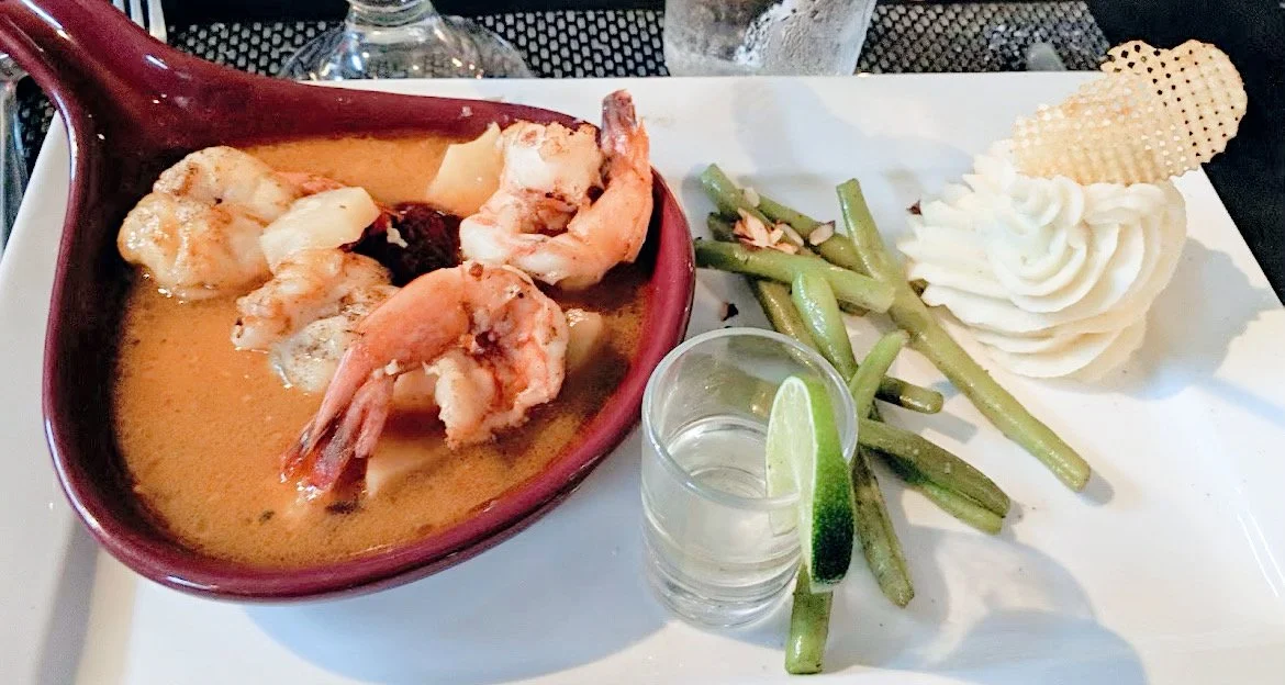 Plated dish featuring shrimp in sauce, green beans with almonds, mashed potatoes, lime slice, and a waffle fry garnish.