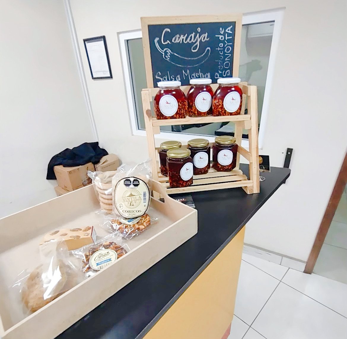 Display of salsa jars and packaged snacks at a counter, with a small chalkboard sign labeled "Caraja Salsa Macha."