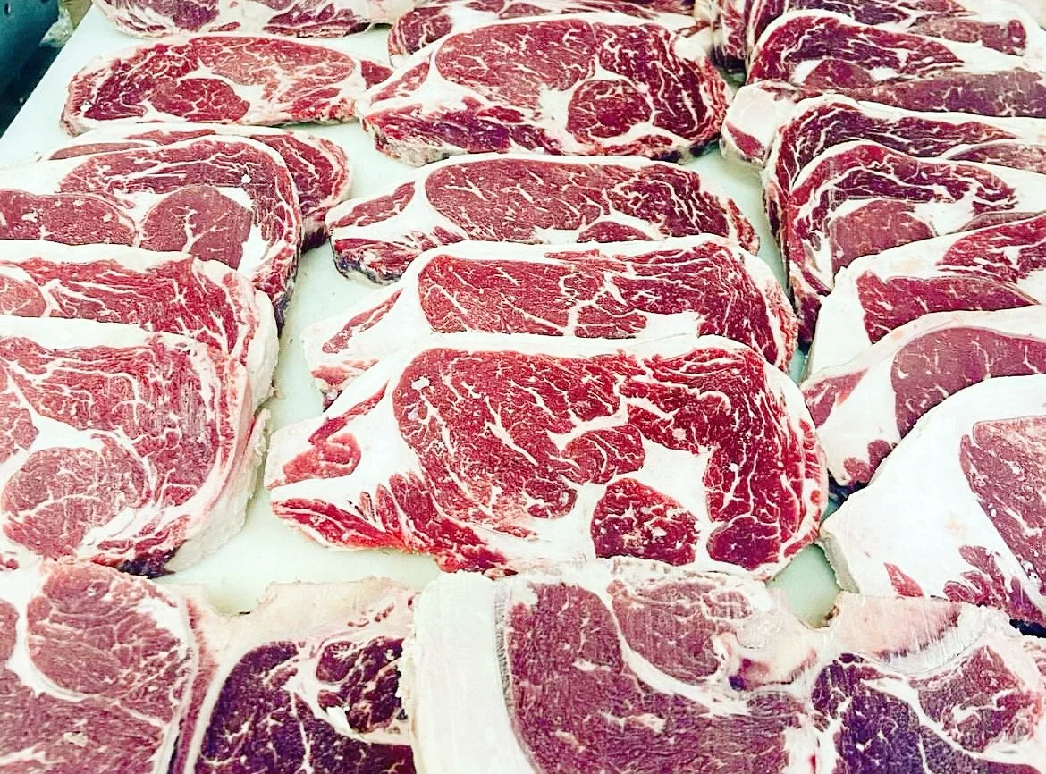 Rows of raw ribeye steaks with marbling, displayed on a white surface.