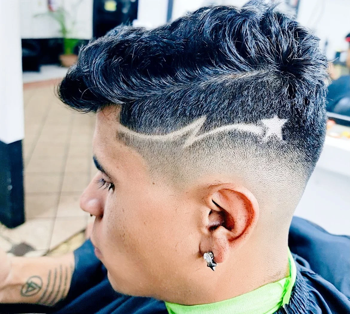 Close-up of a man's side profile with a trendy haircut featuring a star and line design shaved into the side of his head, with an earring visible.