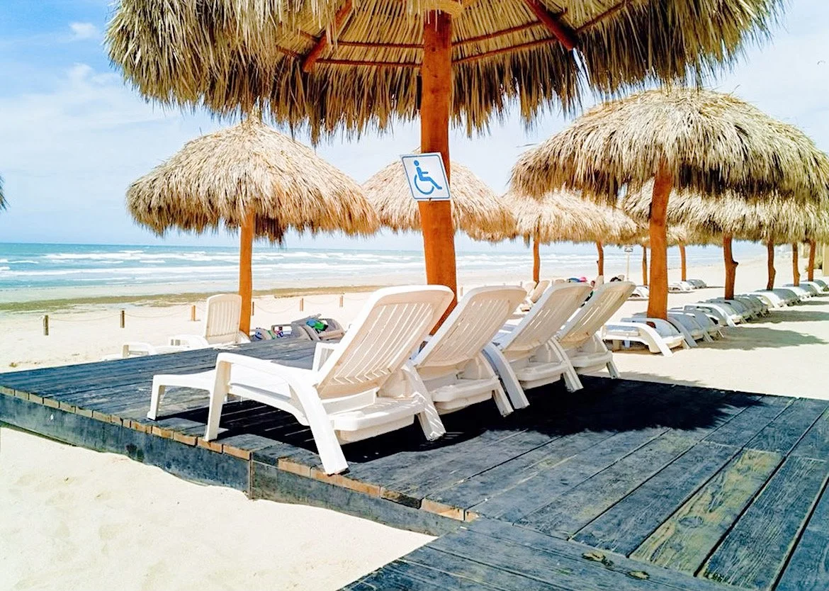 Beach scene with straw umbrellas, lounge chairs on a wooden platform, and a handicap sign, ocean in background
