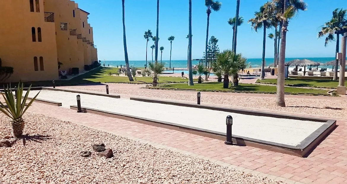 Beachfront hotel with palm trees, a bocce ball court, and a view of the ocean.