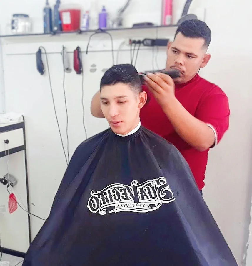 Barber cutting a man's hair in a barber shop with clippers, wearing a red shirt.