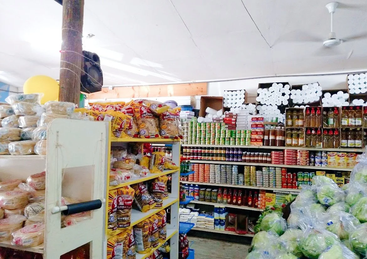 Interior of a grocery store with shelves of packaged tortillas, canned goods, toilet paper, and fresh produce.
