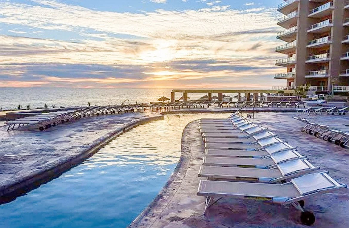 Resort pool area with lounge chairs and ocean view at sunset