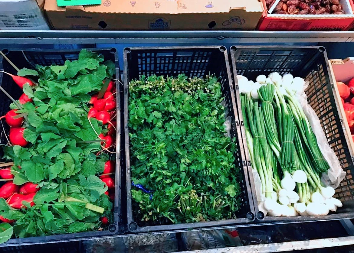 Fresh vegetables in crates, including radishes, cilantro, and green onions at a market.