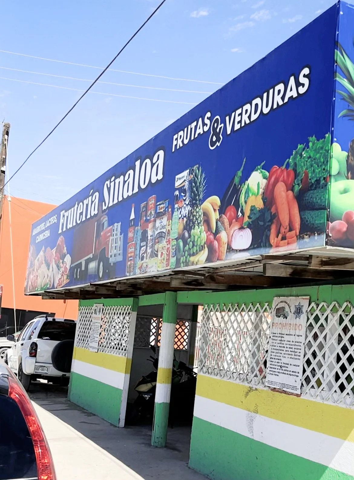 Exterior of a store named Frutería Sinaloa with a sign depicting fruits, vegetables, and grocery items in a colorful display.