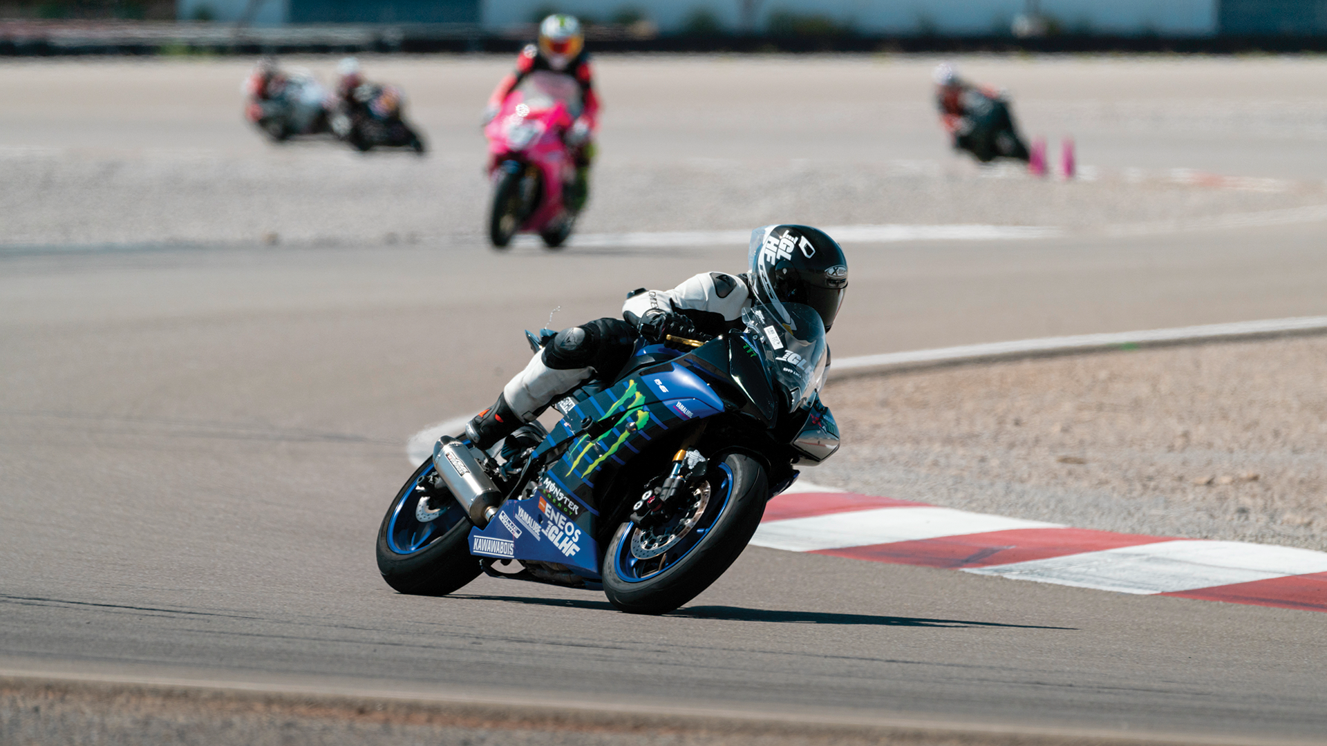 Motorcycle racer leaning into a turn on a race track, with other racers visible in the background.