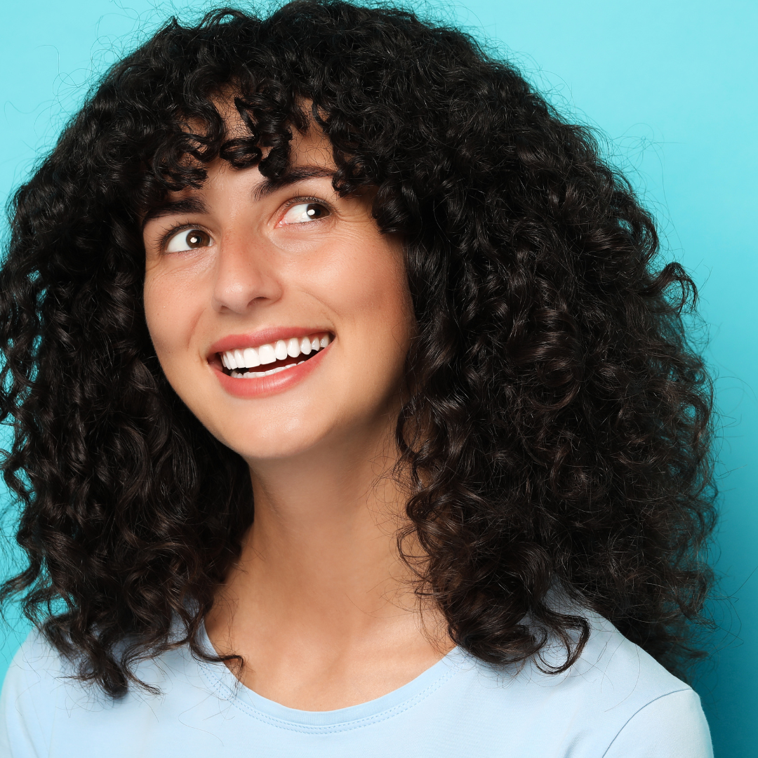 Smiling person with curly hair against a blue background.