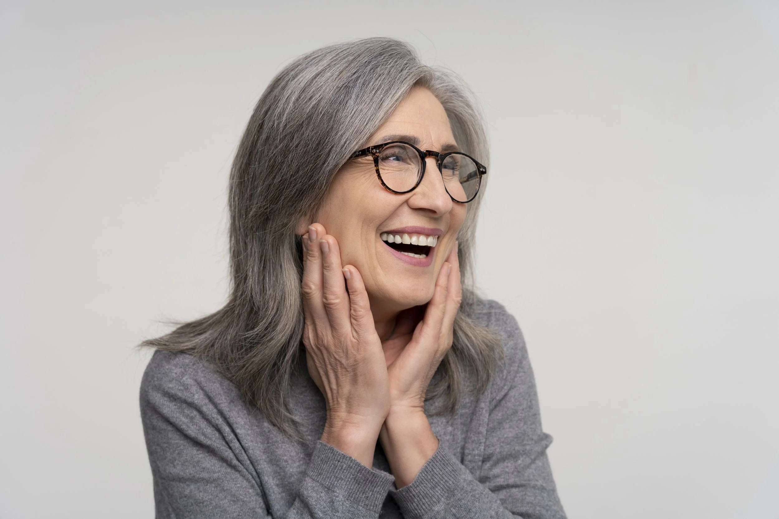 Older woman with gray hair and glasses, smiling, wearing a gray sweater.