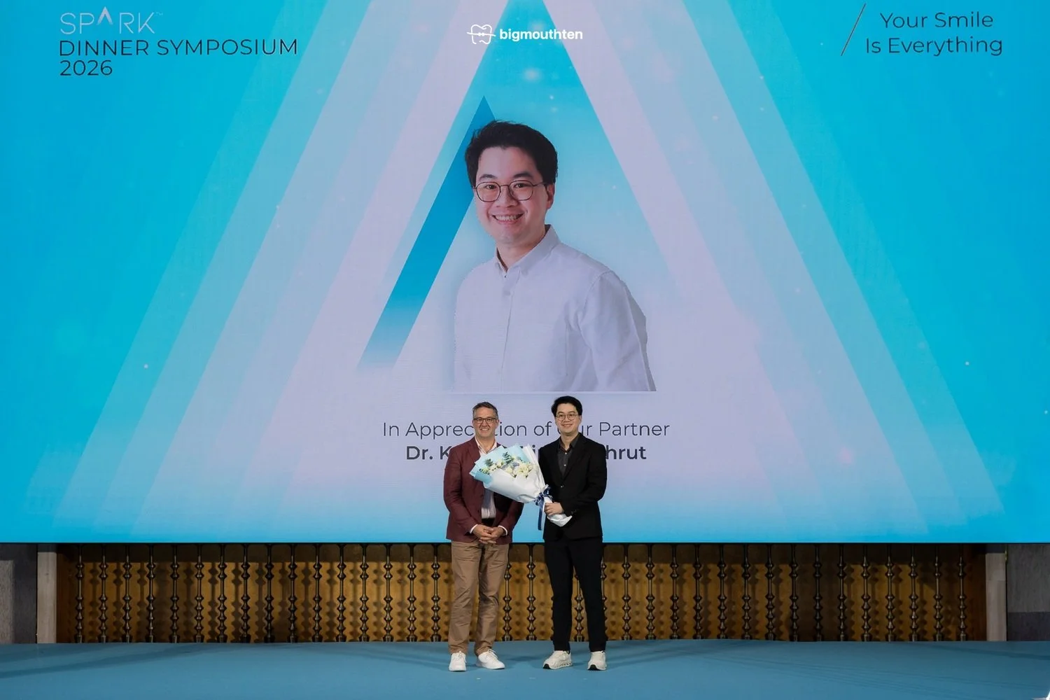 รศ. ทพ. ดร. คณิช ตรีภูวพฤทธิ์ รับช่อดอกไม้แสดงความขอบคุณจากผู้แทน Spark Clear Aligners บนเวทีงาน SPARK Dinner Symposium 2026
