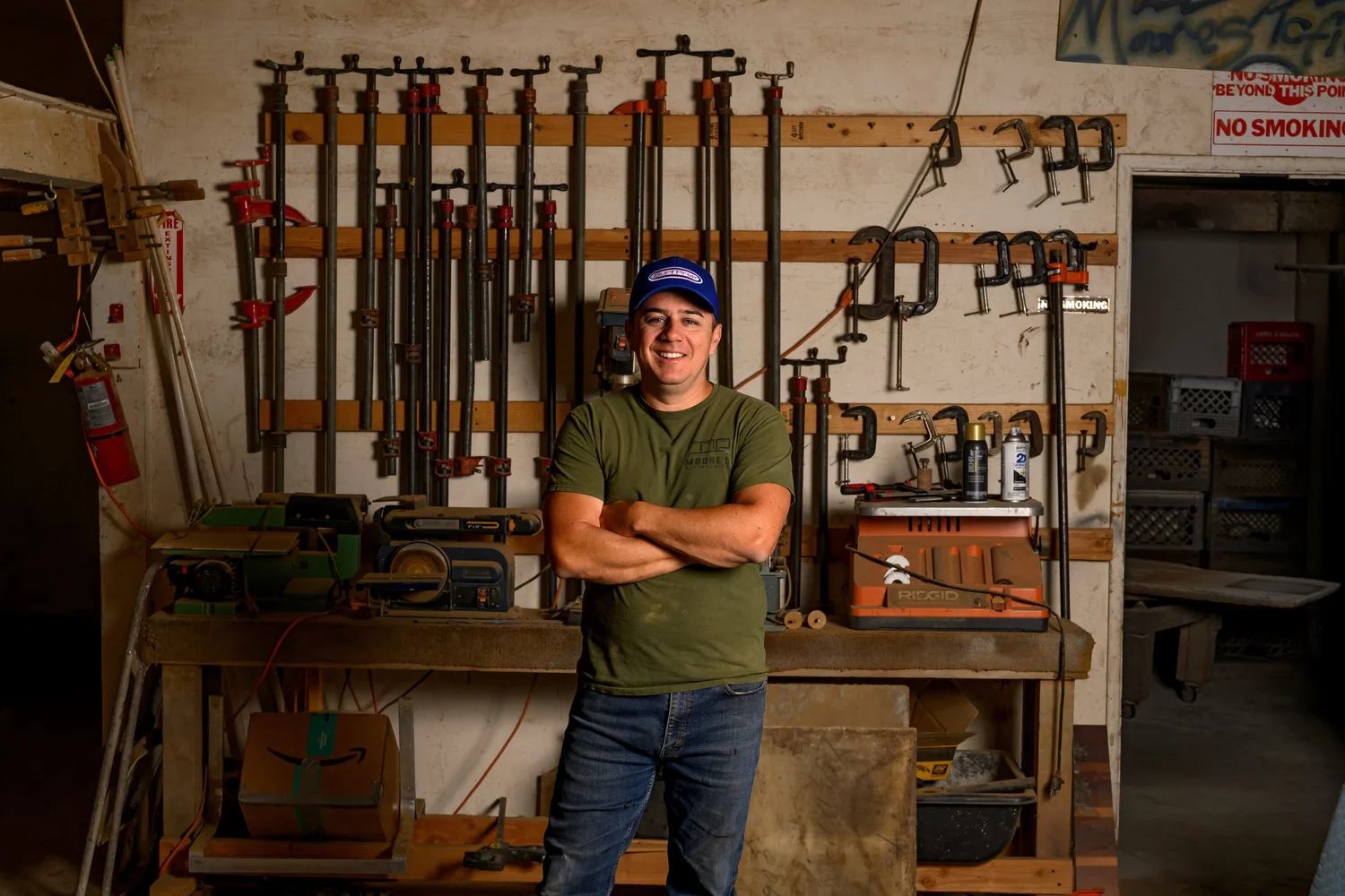 Aaron Moore, arms crossed, in front of the clamp wall in his shop
