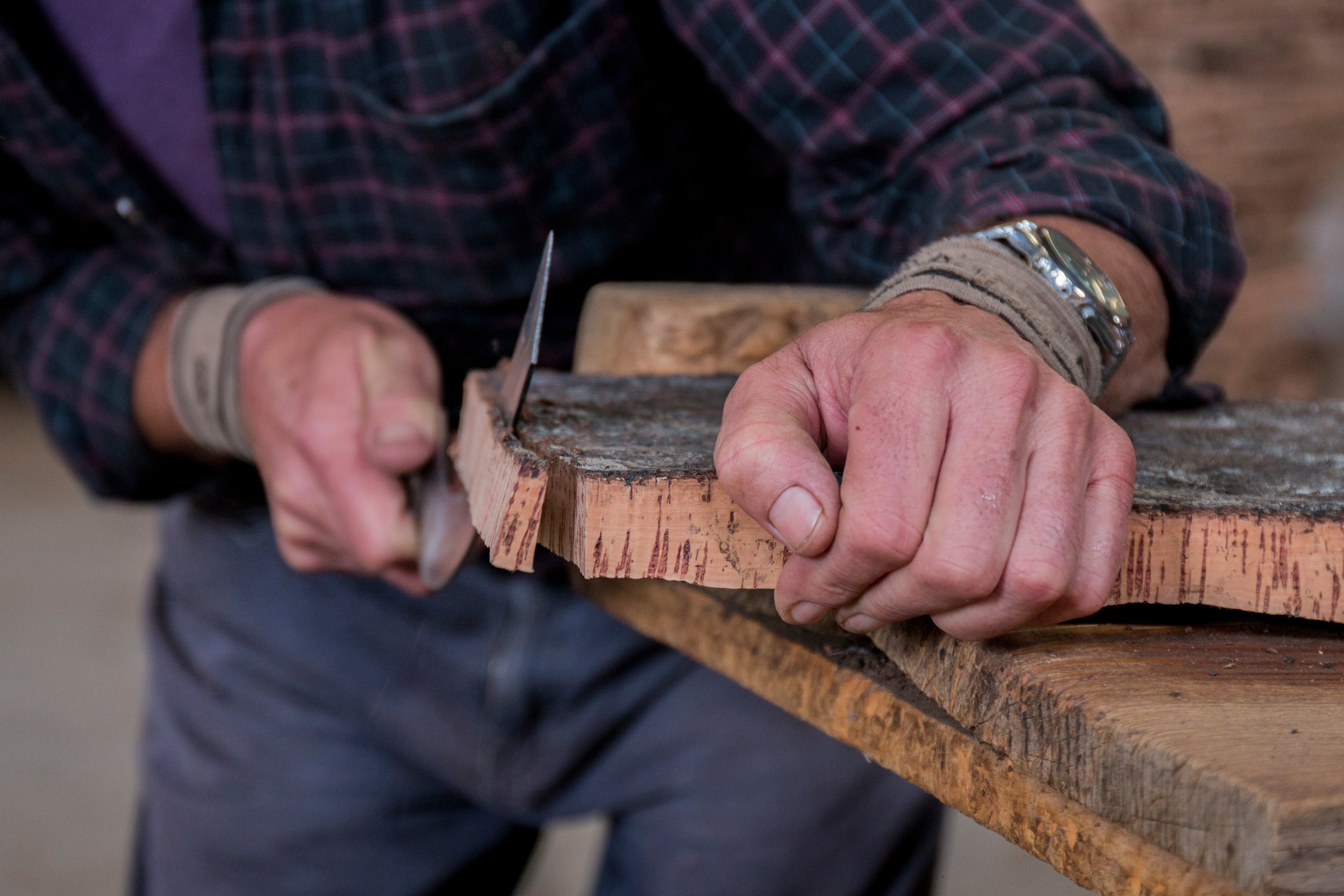 Person, die ein Stück Holz mit einer Handsäge zersägt, trägt ein kariertes Hemd und Armbänder.