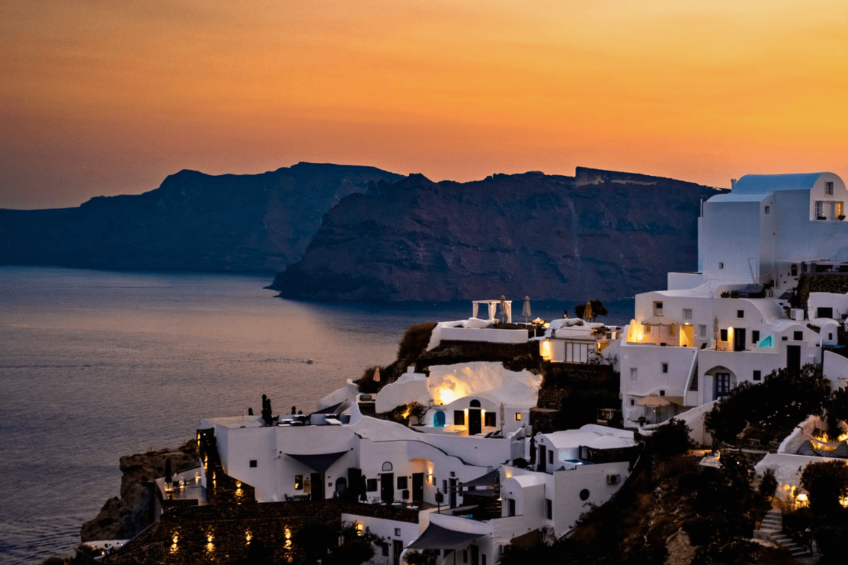 Santorini caldera at sunset with whitewashed cave hotels and lights along the cliff