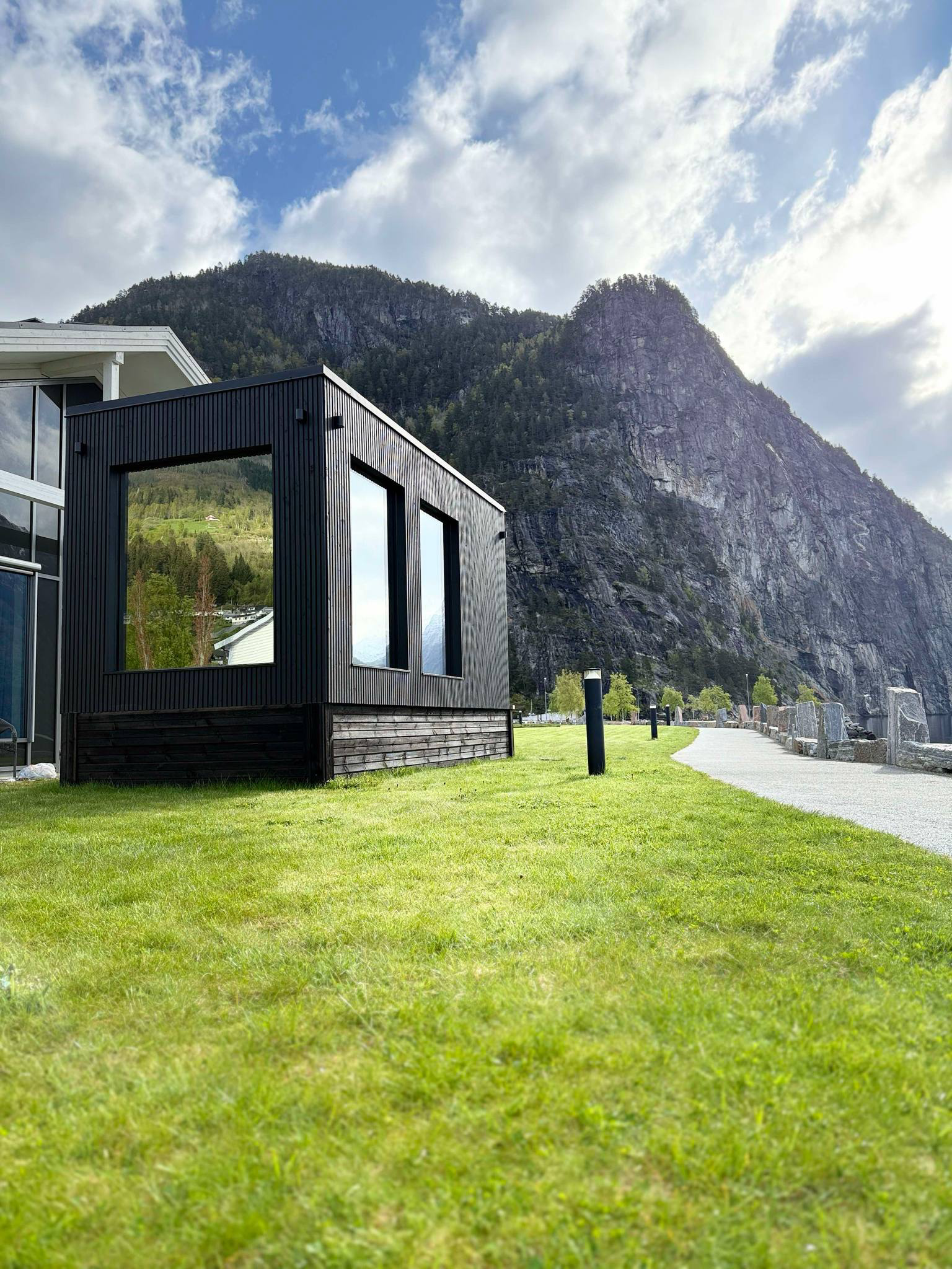 Moderne svart bygning med store vinduer ved fjellandskap og grønt gress.