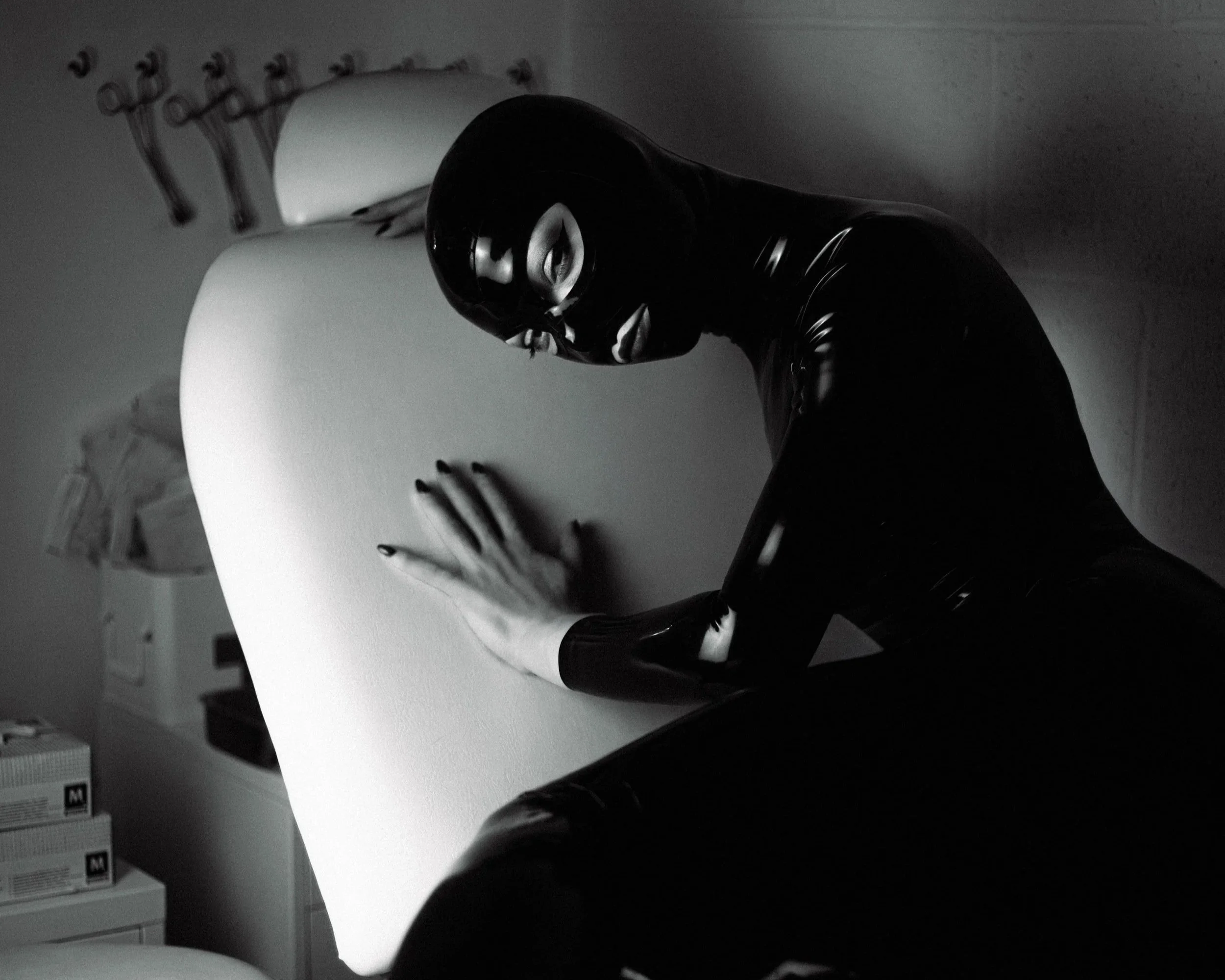 Person wearing black gloves and a mask sitting at a white table with a white cup, with a blurred background.