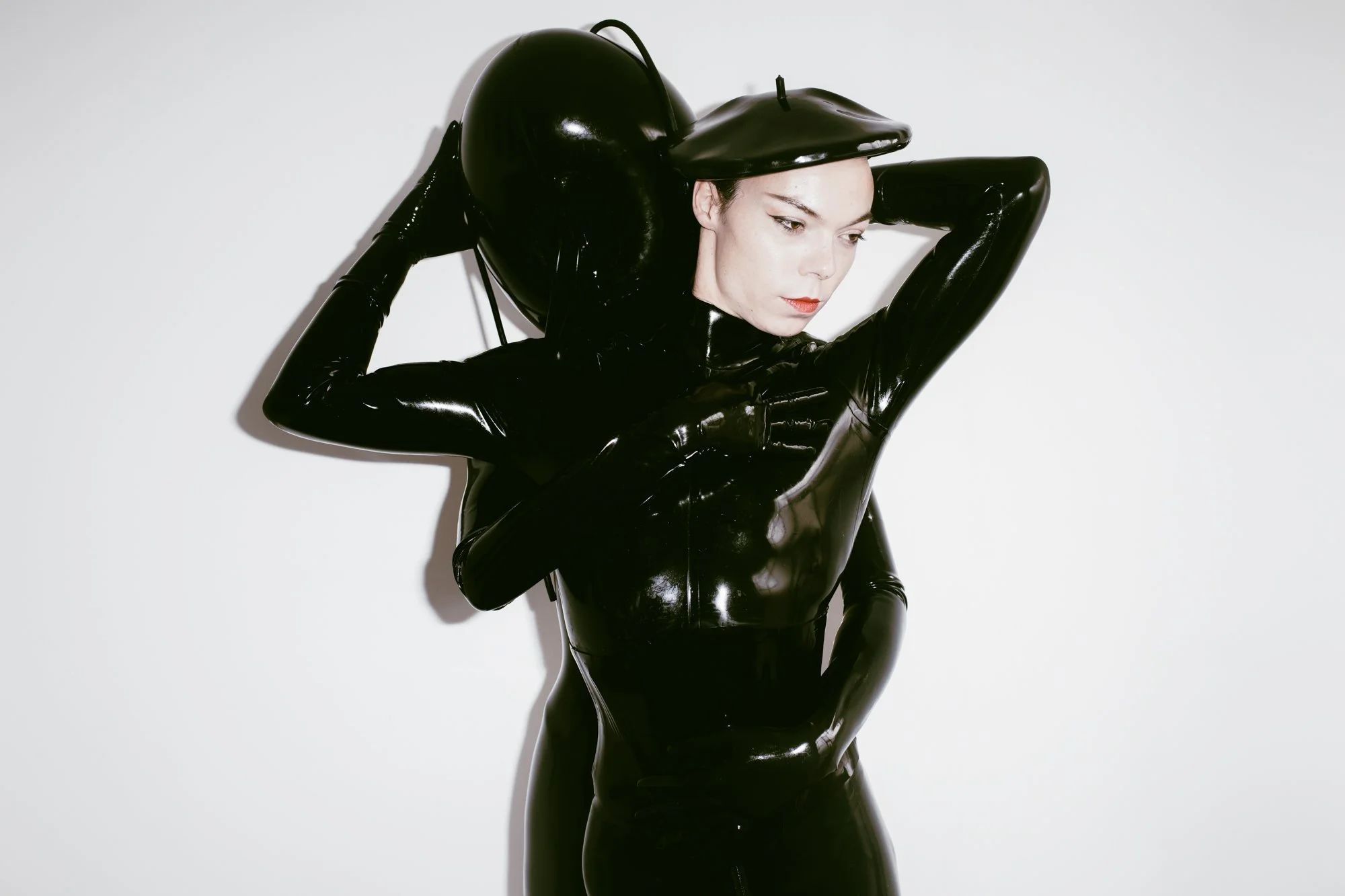 A modern house with wood and metal exterior, large glass window, situated in a mountainous landscape with dry grass and small trees.