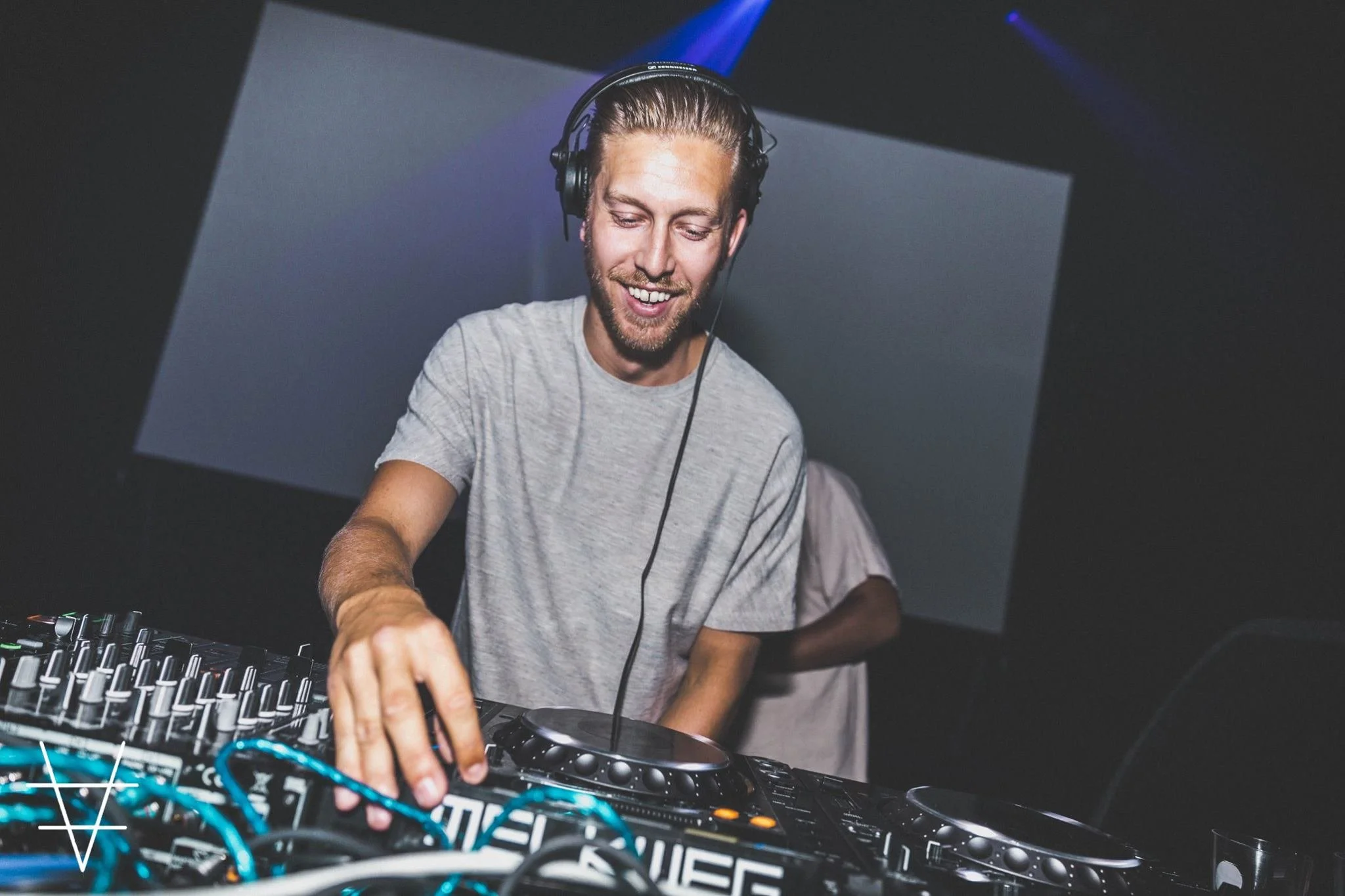 A young man with headphones smiling while DJing at a music event.