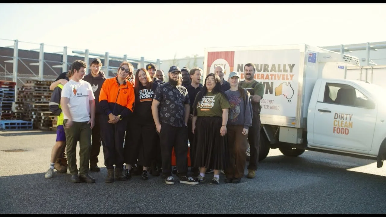 Group of people standing in front of a truck with the logo 'Dirty Clean Food' and a message about better food for a better world.