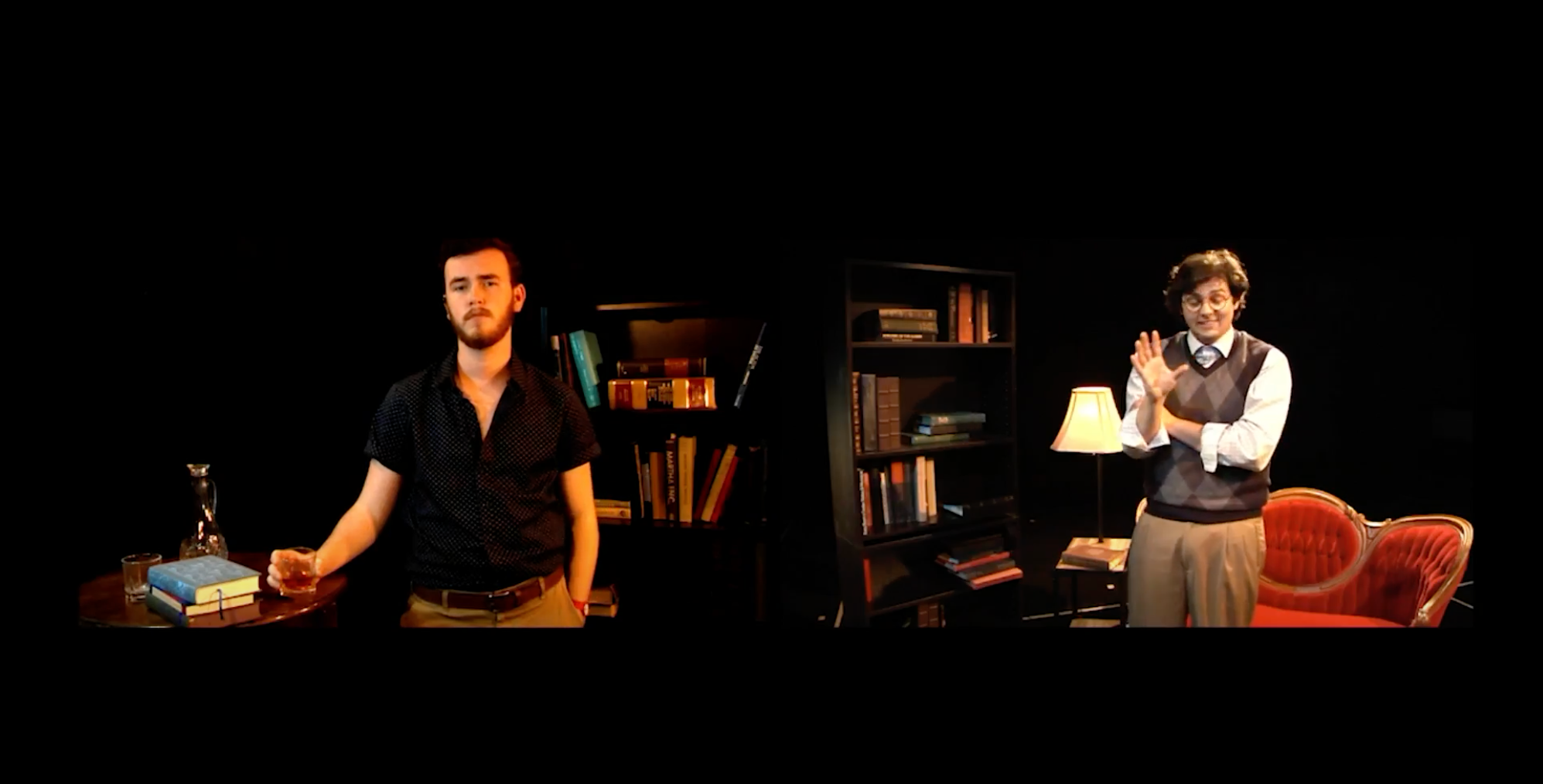 Two men in a room with dark background and furniture. The man on the left has a beard, wearing a black shirt, holding a drink. The man on the right wears glasses, a sweater vest, and a tie, standing near a red sofa and bookshelf, clapping and smiling