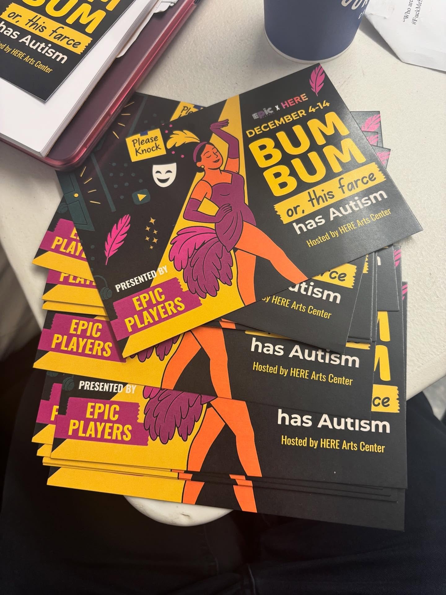 Flyer for an event titled 'Bum Bum or this farce has Autism,' hosted by HERE Arts Center, presented by Epic Players, with colorful illustrations of a person in a purple dress and pink feathers, on a table with other flyers and a cup.