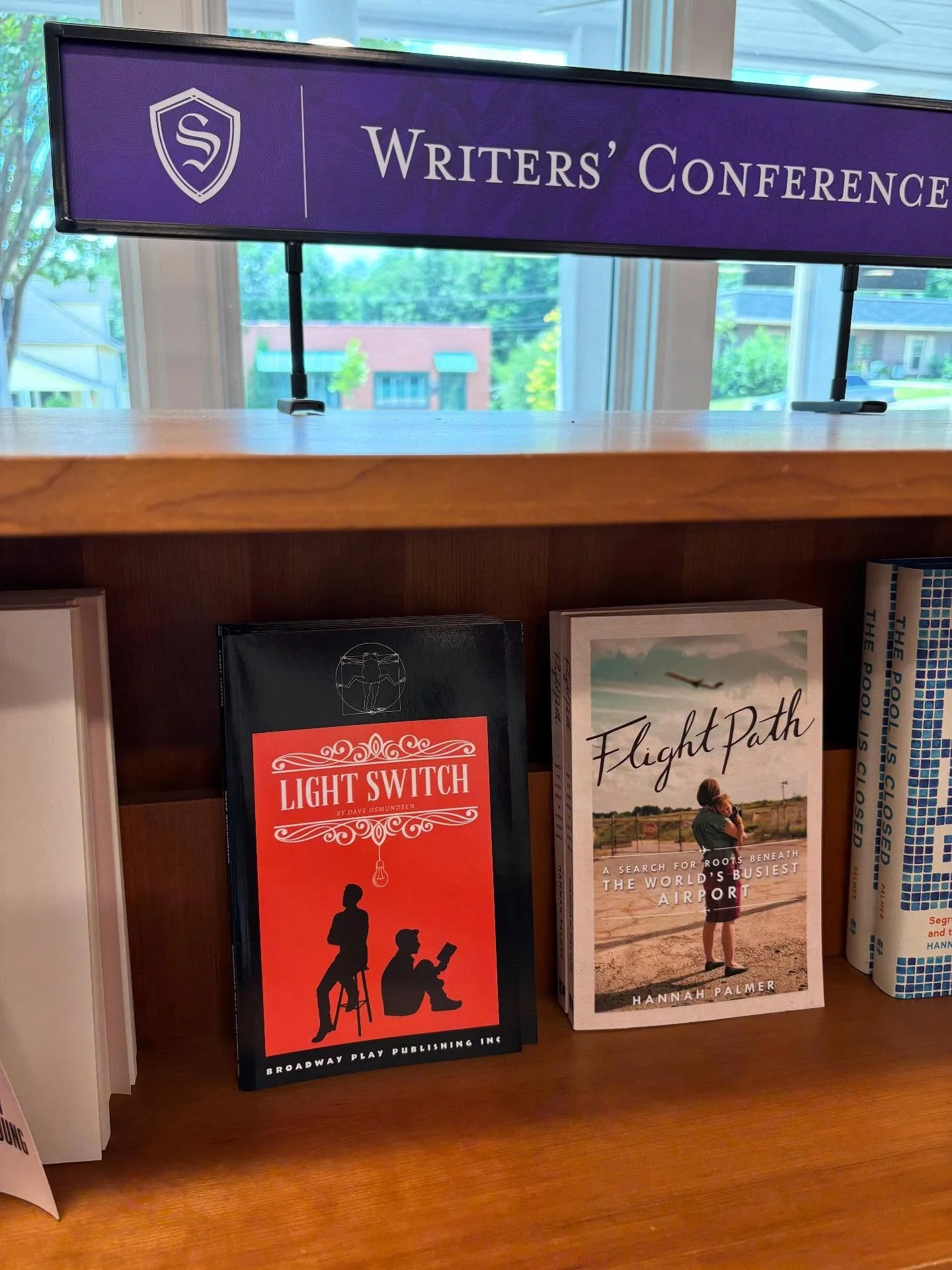 Bookshelves with book titles 'Light Switch' by Dave Osmunson and 'Flight Path' by Hannah Palmer on a wooden shelf, with a