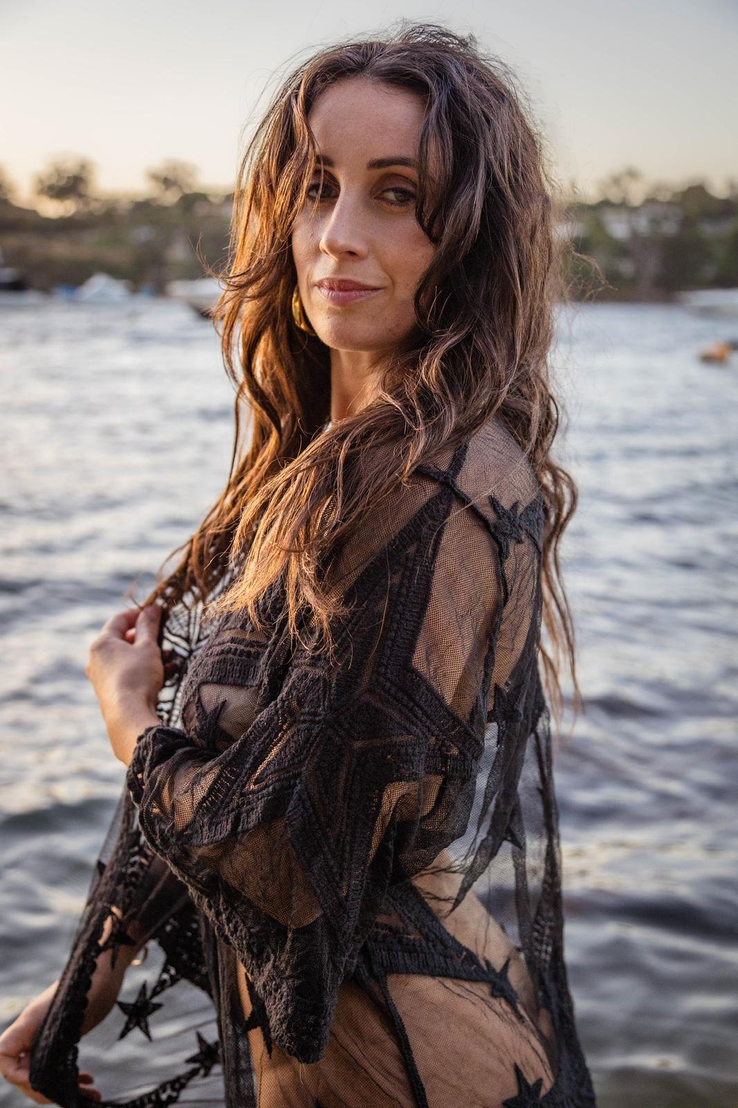 Woman in sheer black cover-up by the water at sunset