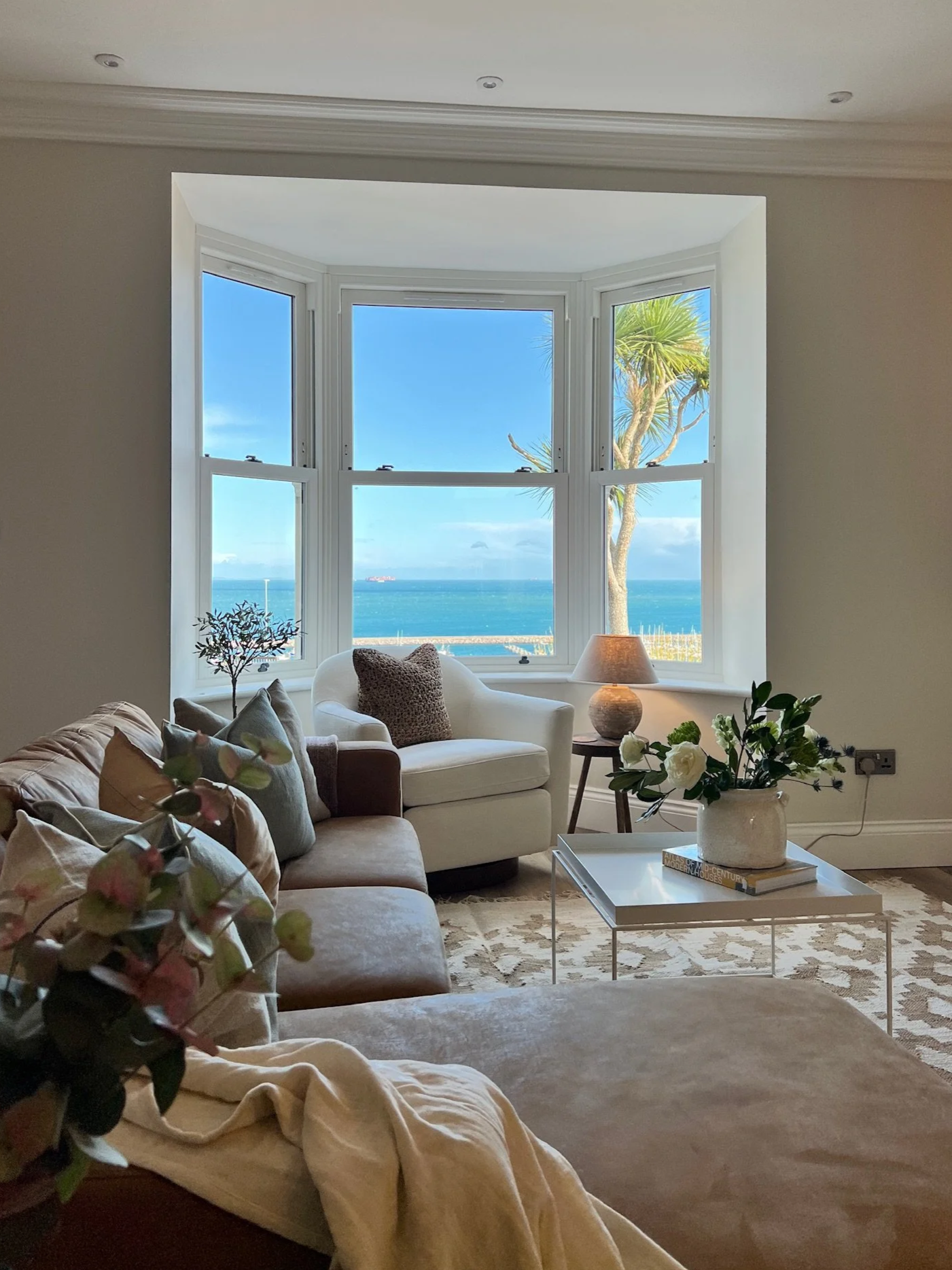 Coastal living room in Project Brixham, Devon, featuring soft neutral interiors, a bay window with sea views and timeless styling by Istigh Interiors.