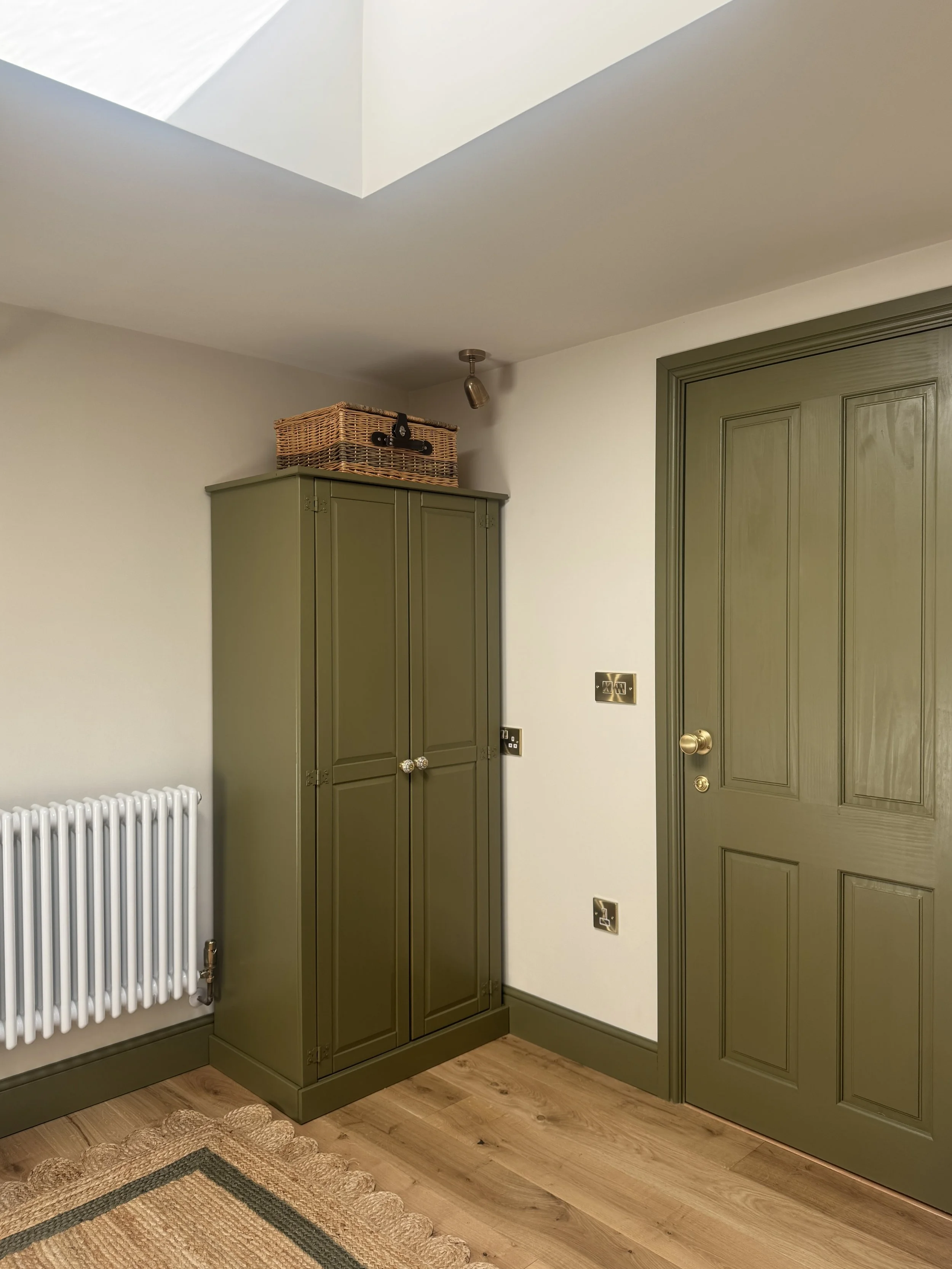 Colourful joinery and woodwork with warm oak flooring and traditional radiator in a light filled bedroom with skylight.